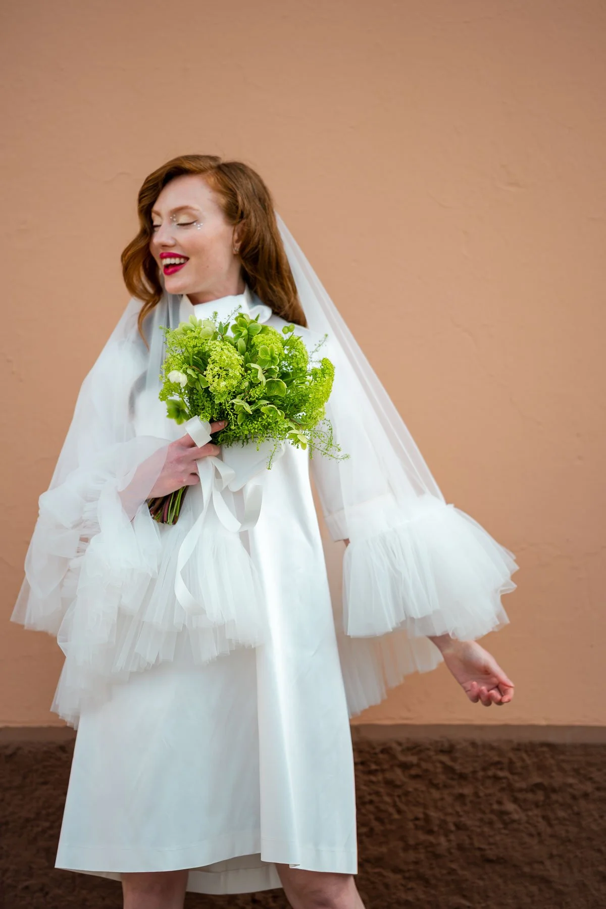 En kvinne i hvit brudekjole holder en grønn blomsterbukett og smiler
