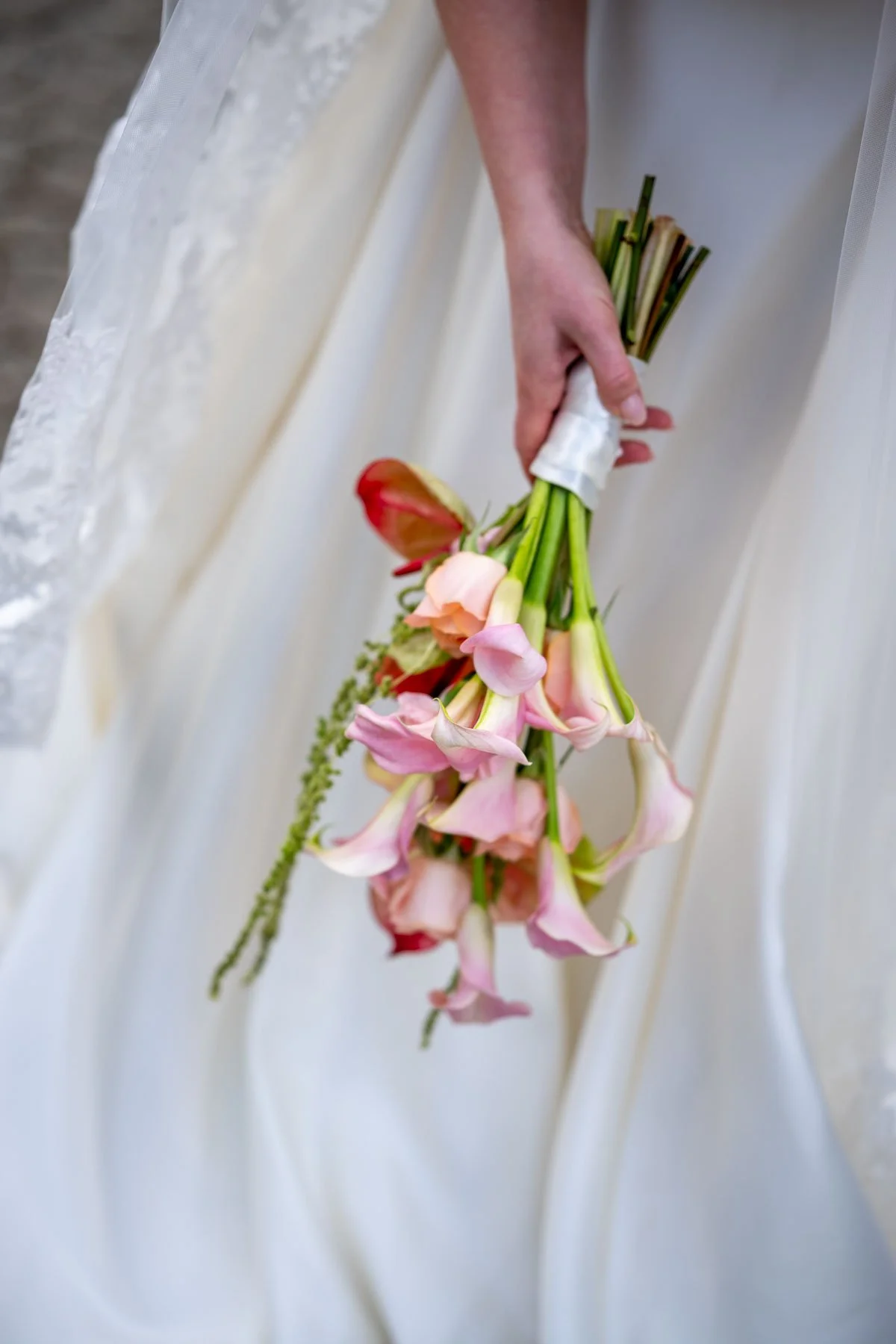 Person holder en bukett med blomster i en hvit brudekjole.