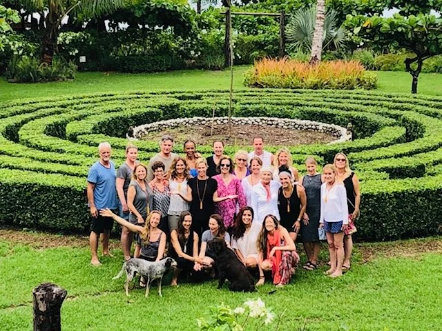 Group of people posing outdoors in front of a circular hedge garden with green grass and trees in the background.