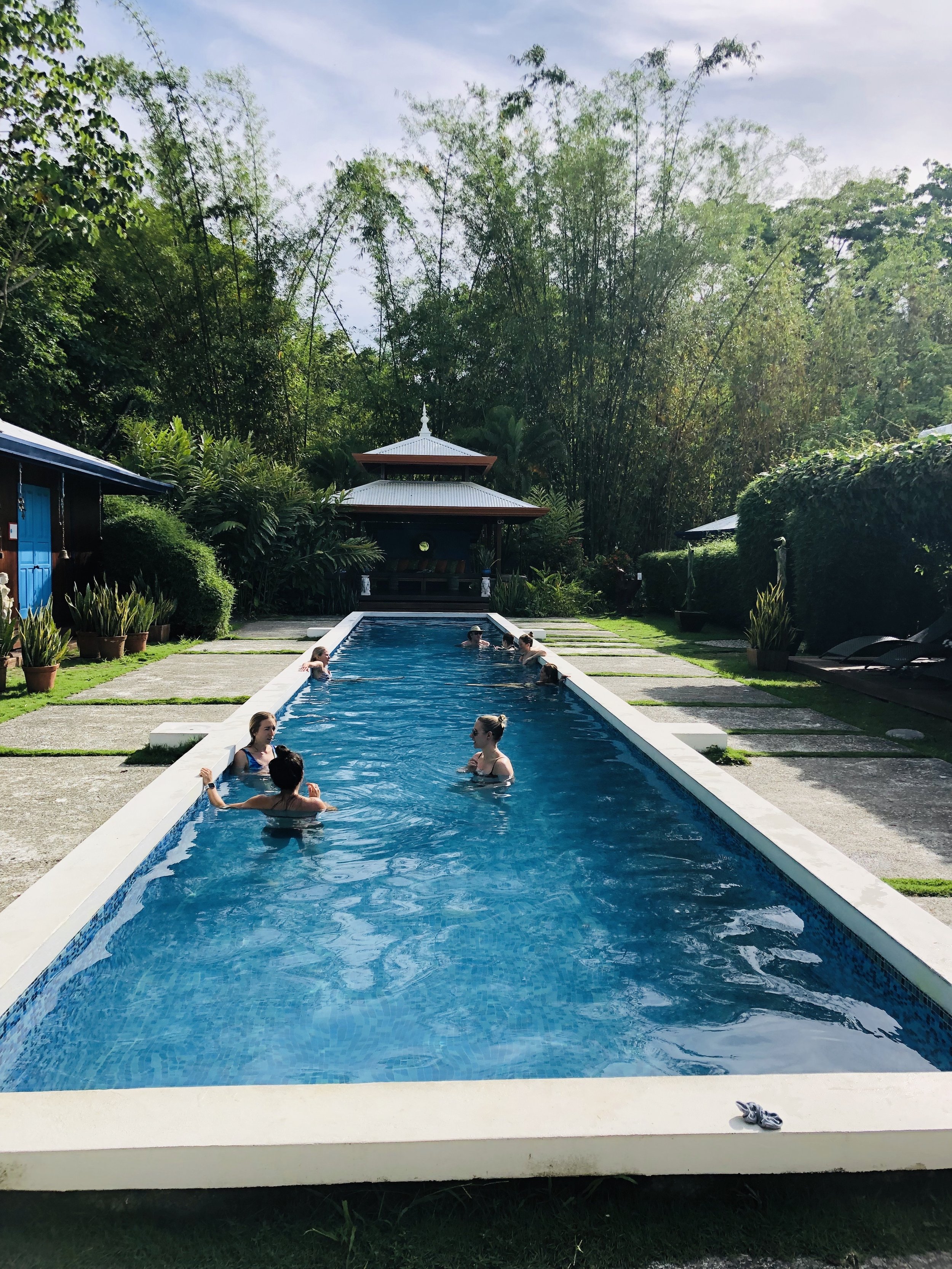 People swimming and relaxing in a rectangular outdoor pool surrounded by greenery and a traditional pavilion in the background.
Yoga retreat in Costa Rica led by Vivica Schwartz. 
