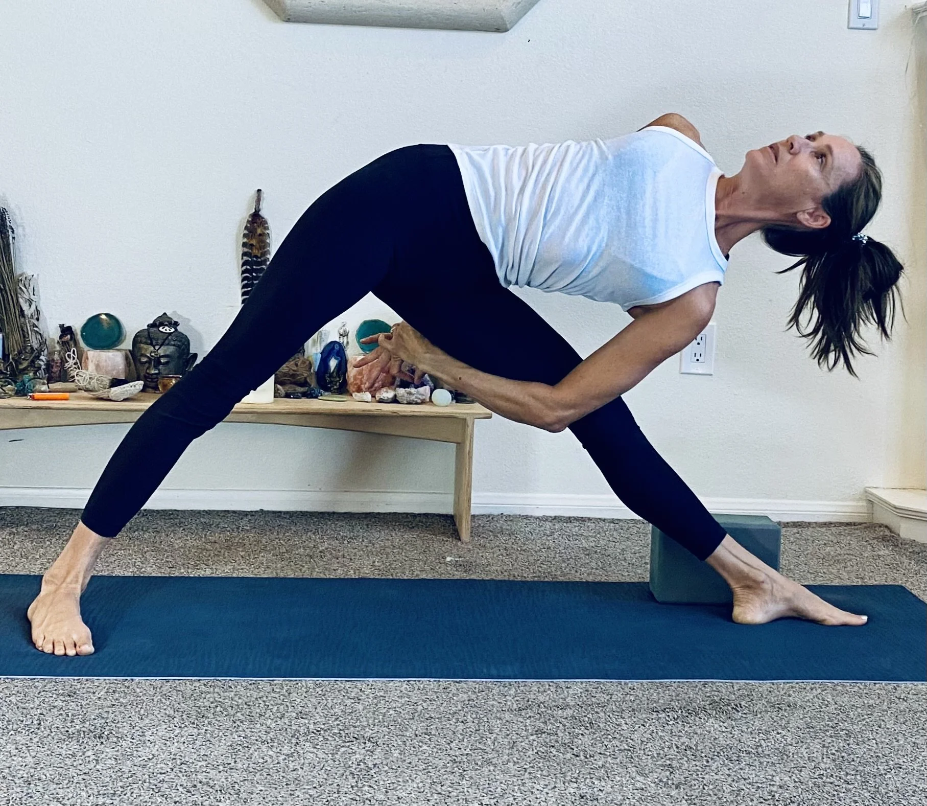 Vivica Schwartz practicing yoga poses in a room with a shelf of stones and spiritual objects on a wooden table in the background.