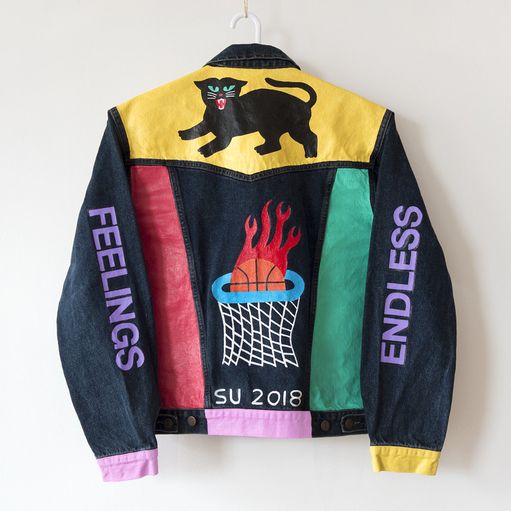 A photo of a leather jacket that is painted. It has the words "endless" on one sleeve and "feelings" on the other, a black panther on the top panel, and a basketball hoop with a flaming basketball going through it.