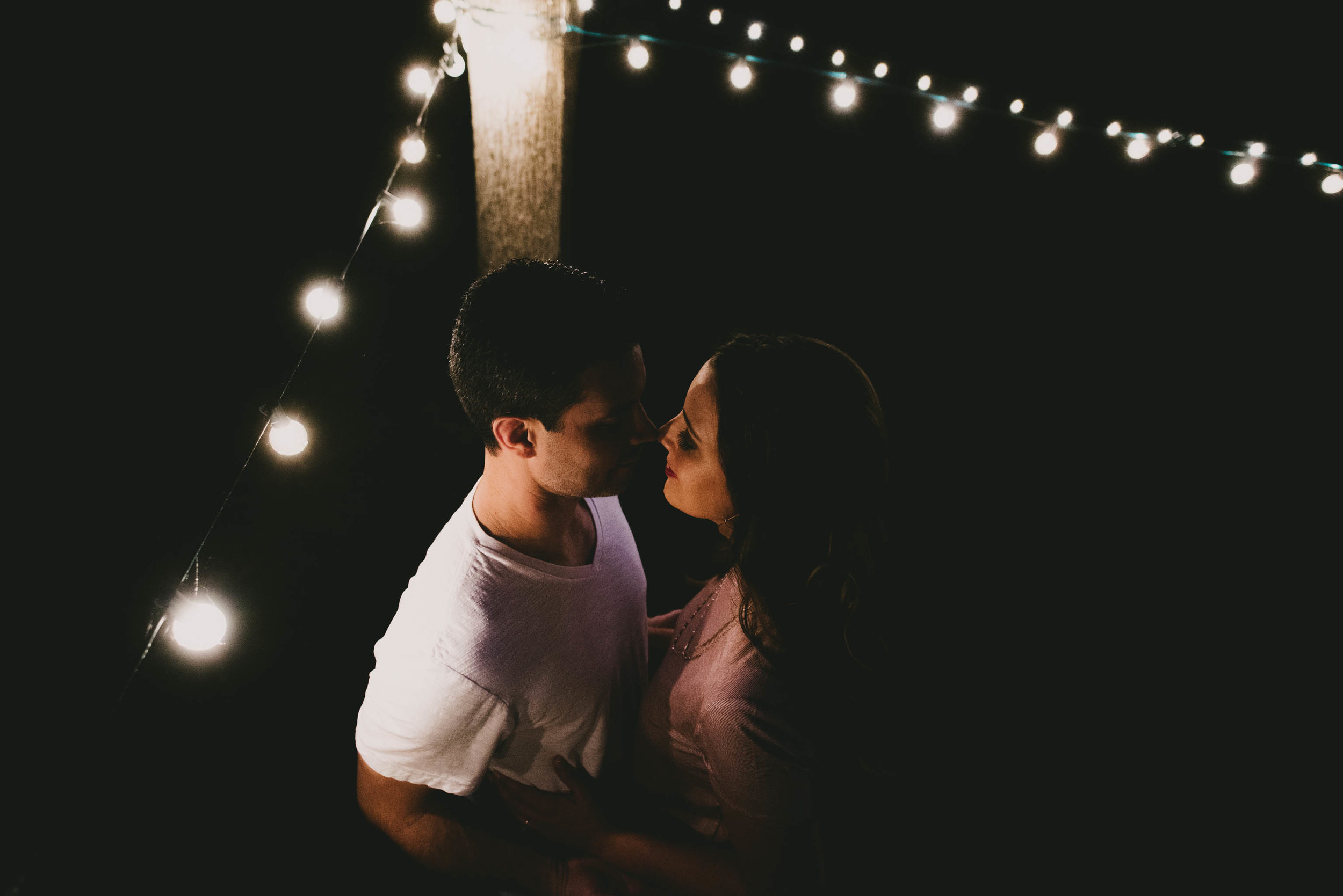 couple under market lights in their back yard during their engagement session in Durham, North Carolina