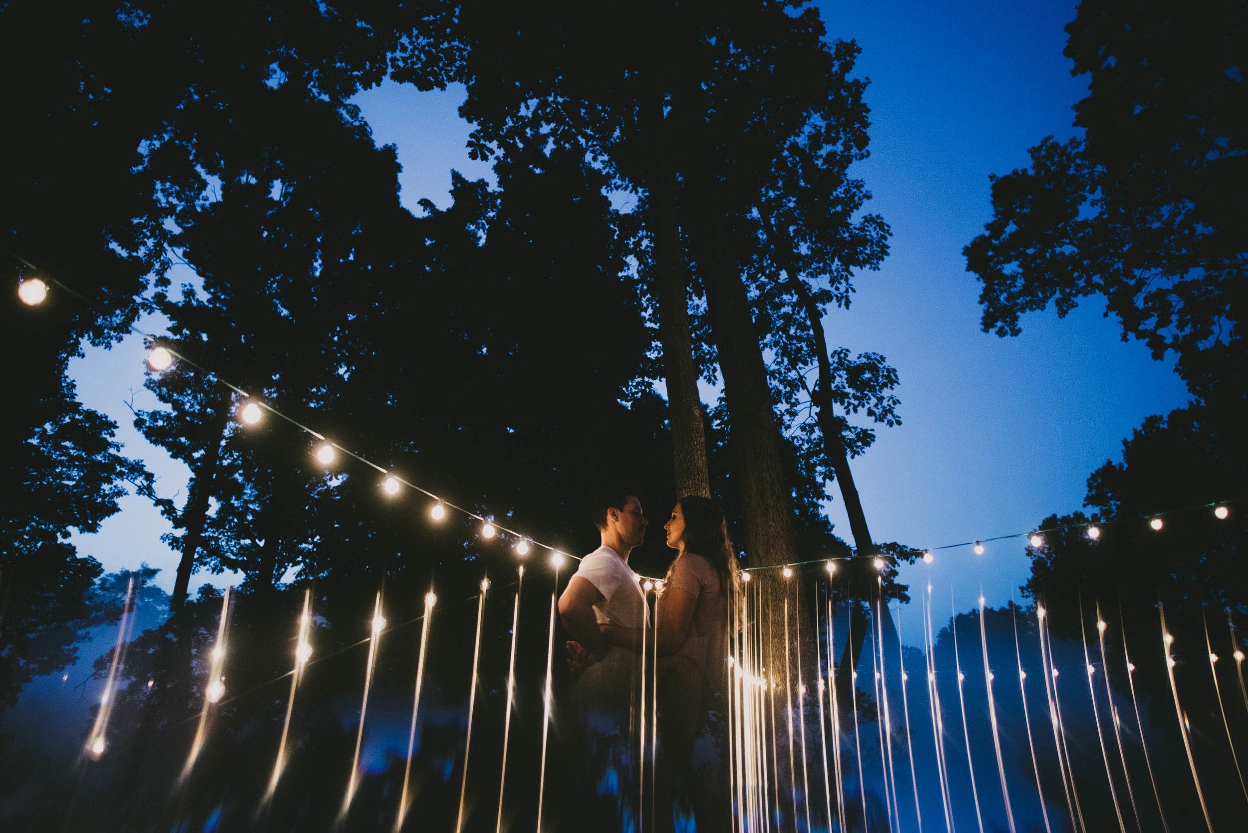 couple surrounded by reflection of market lights, sky and trees during their engagement session in Durham, North Carolina