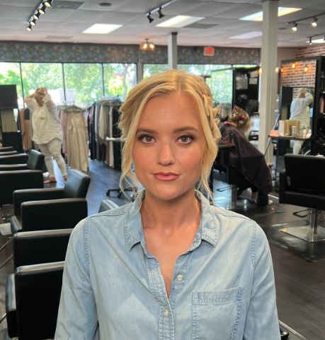 A young woman with blonde hair and a denim shirt sitting in a clothing boutique or salon.