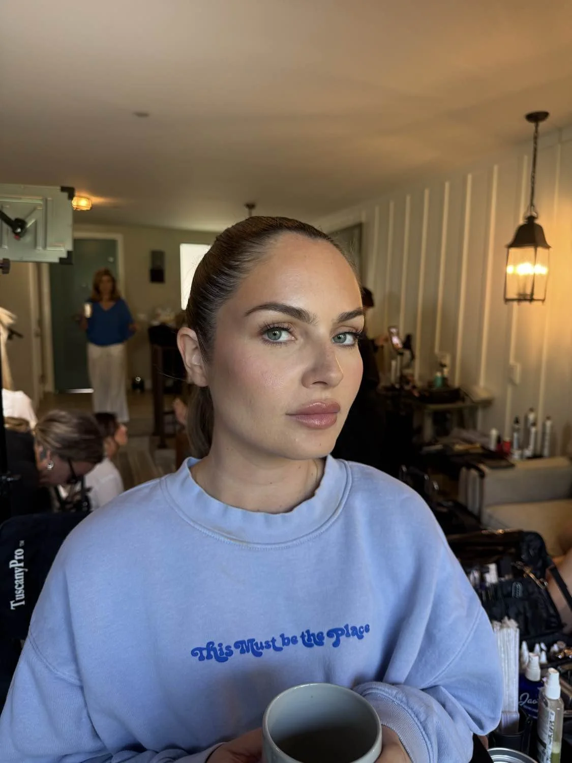 Young woman with blue eyes and makeup holding a mug in a salon or makeup studio.