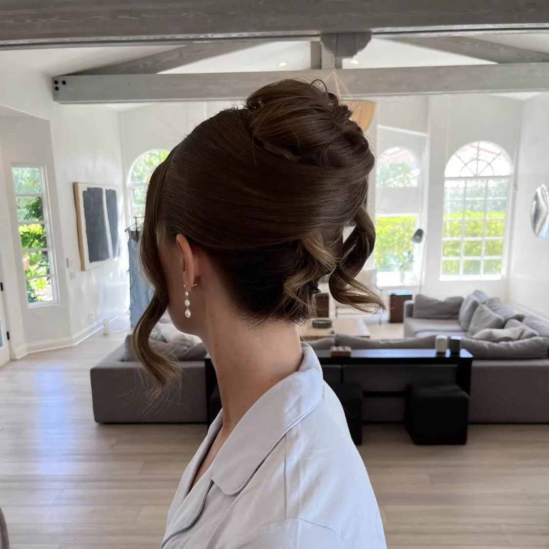 Woman with elegant updo hairstyle wearing pearl earrings inside a bright, modern living room