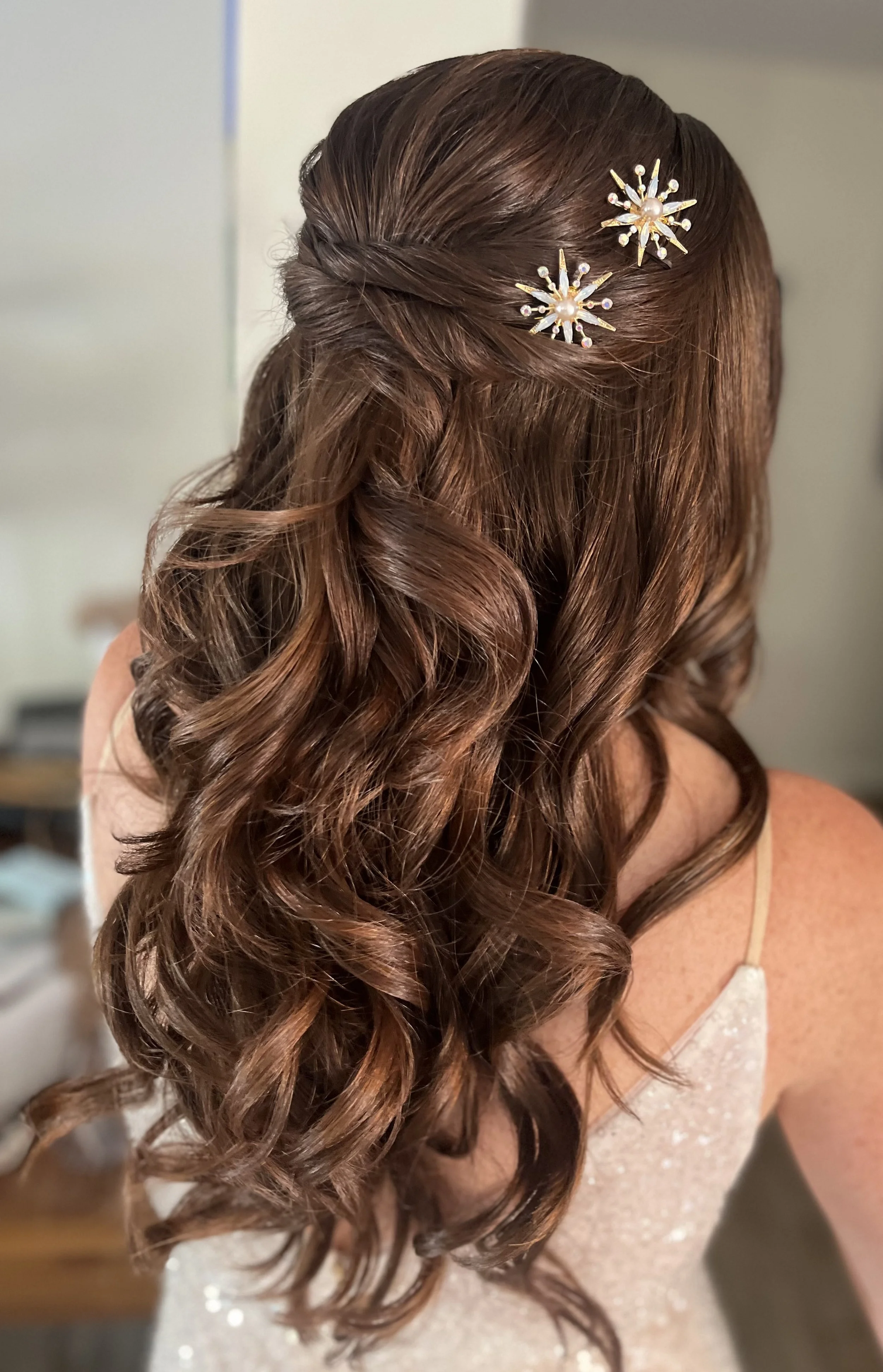 Back view of a woman with long, curled brown hair styled with two decorative pearl and crystal hair clips in a starburst design.