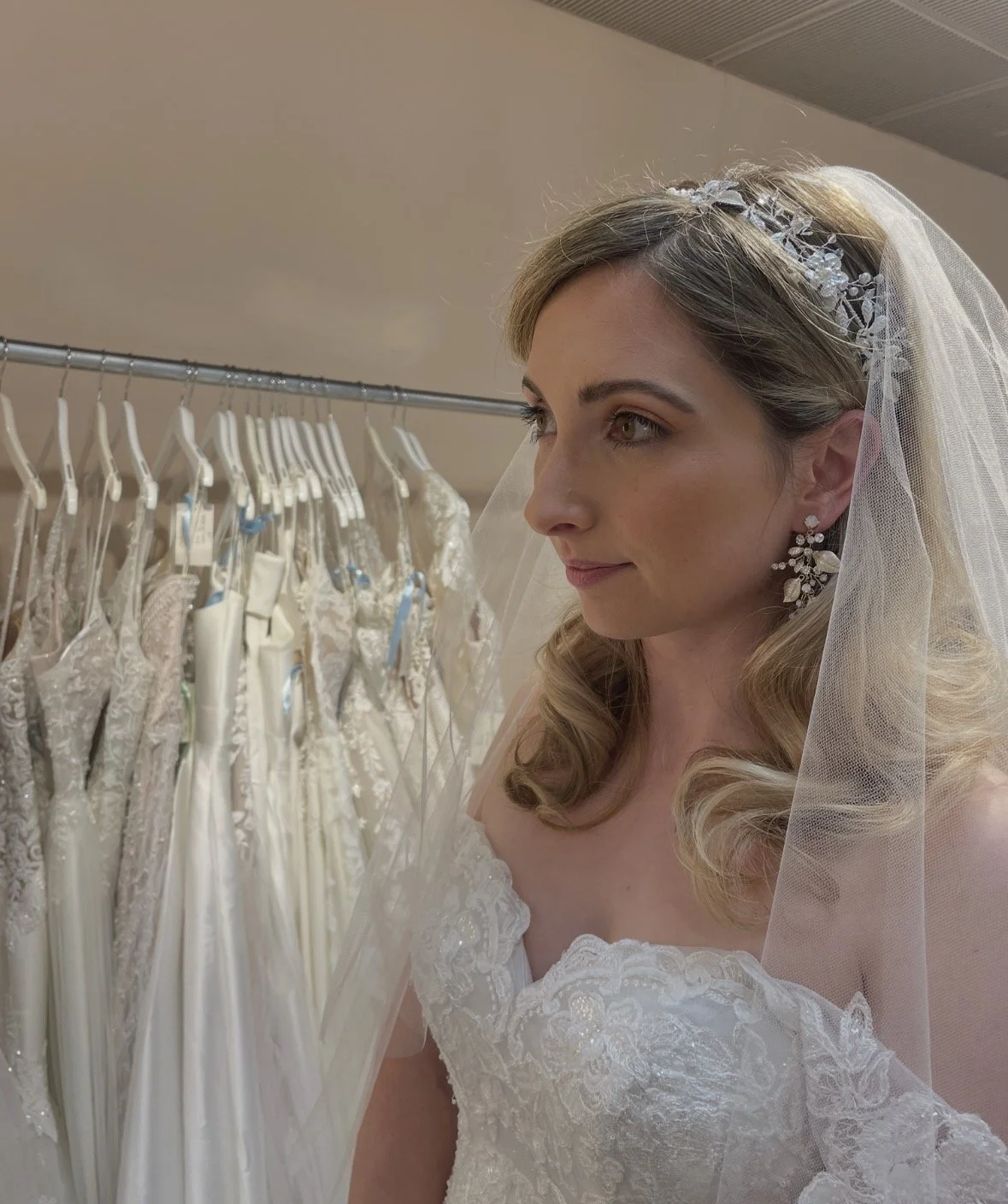 A bride trying on a wedding dress, looking at a rack of white wedding gowns.