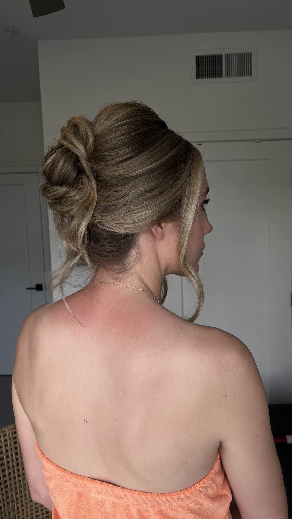 Side view of a woman with styled blonde hair in an updo, wearing an orange strapless dress.