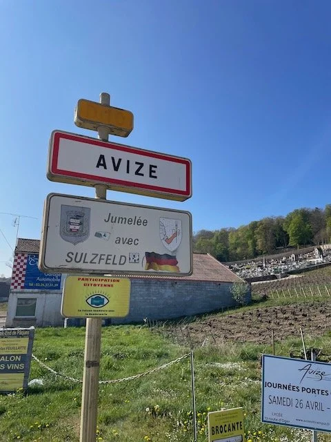Avize village entrance sign in the Côte des Blancs, Champagne — Grand Cru Chardonnay village with chalky vineyards visible on the hillside behind