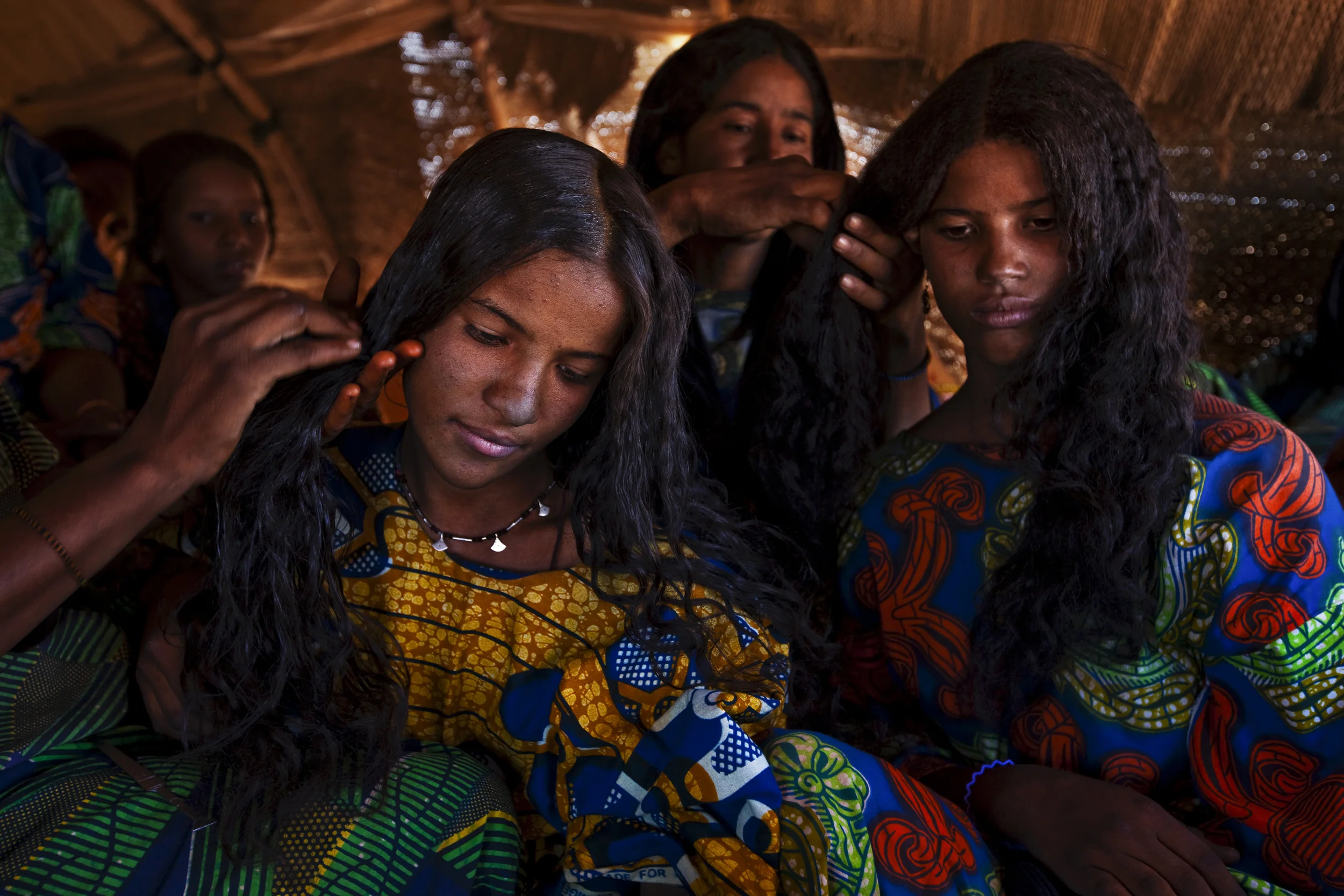 INGAL, NIGER, OCTOBER 2009: Two young Tuareg women have their hair dressed by other Tuareg women inside a traditional nomad tent at a Tuareg Nomad camp, Ingal Region, Niger, 11 October 2009. Tuareg Nomads have two traditional priorities, their animals and access to water. This group has moved to this region at this time to enjoy the remaining good grassland of the rainy season and will soon move again to be close to a good water source. The nomads survive on a diet of millet and camel milk which is occasionally supplemented by goat meat. (Photo by Brent Stirton/National Geographic.)