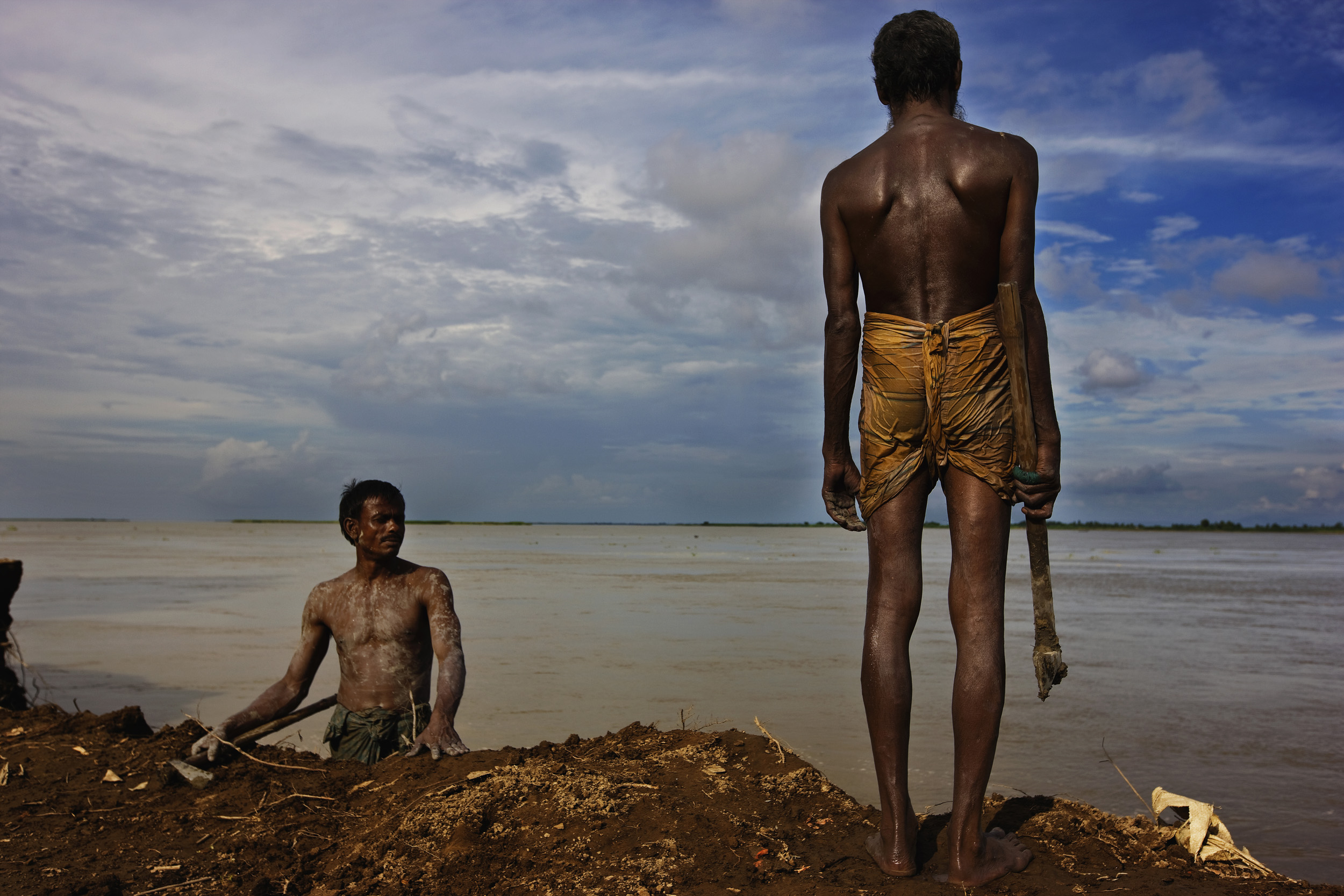 KURIGRAM, BANGLADESH-AUGUST 2008: Flood affected village men hack away the embankment left by the most recent flooding in the area where their village used to be, Kurigram, Northern Bangladesh, 2 August 2008. They are doing this on the orders of the