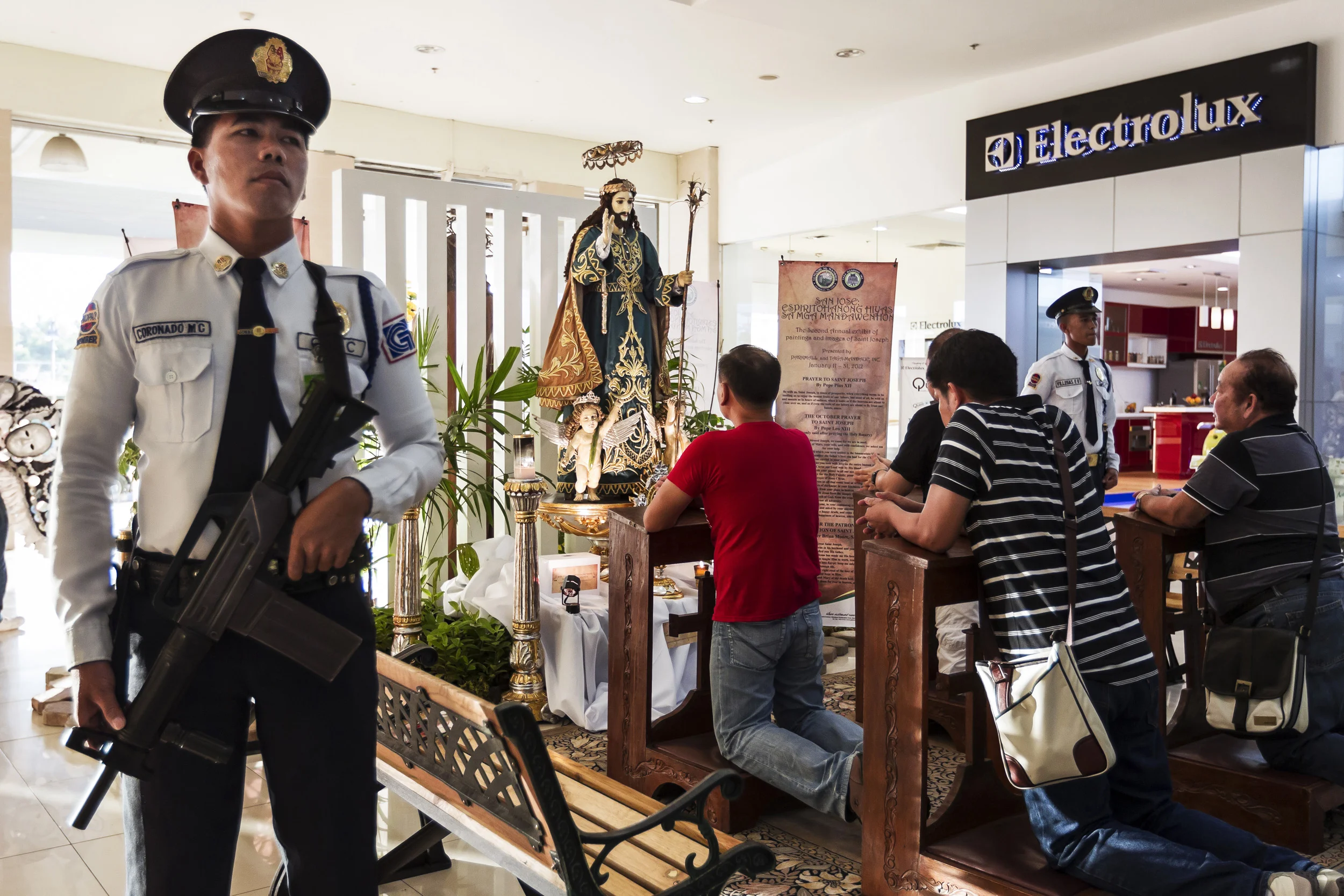 CEBU, PHILIPPINES, JANUARY 2012: Armed security guards watch over an ivory carved St Joseph statue on display at a religious exhibit in Park Mall shopping center, Cebu, Philippines, January 19, 2012. There is a space to pray in front of the statue and there are also many other smaller icons on display. This is the largest Ivory carved statue of St Joseph in existence. There is a collective of wealthy collectors in the Philippines who both search out and commision new work, thus sustaining a trade which allows for the continuing and growing market for new ivory. This has an inevitable effect on threatened elephant populations worldwide, accelerating demand for a commodity which is growing in value. This feature is about representing a global picture through a new and unseen lens. It places an onus of responsibility on an influential religious and wealthy elite. It offers them the chance to acknowledge their influence for good in the face of accelerating losses that are non-recoverable. It furthermore allows them to do so in the name of a value system integral to their expoused beliefs. It simply requires a reversal of priorities, from one that places iconography above life, to one that places life about iconography. This preaches a new message of compassion for all life, all God’s life, and ultimately benefits the protagonists and allows them to emerge not only unscathed but reinvigorates their standing as leaders in the value system their religious sector expouses. (Photo by Brent Stirton/Reportage for National Geographic.)