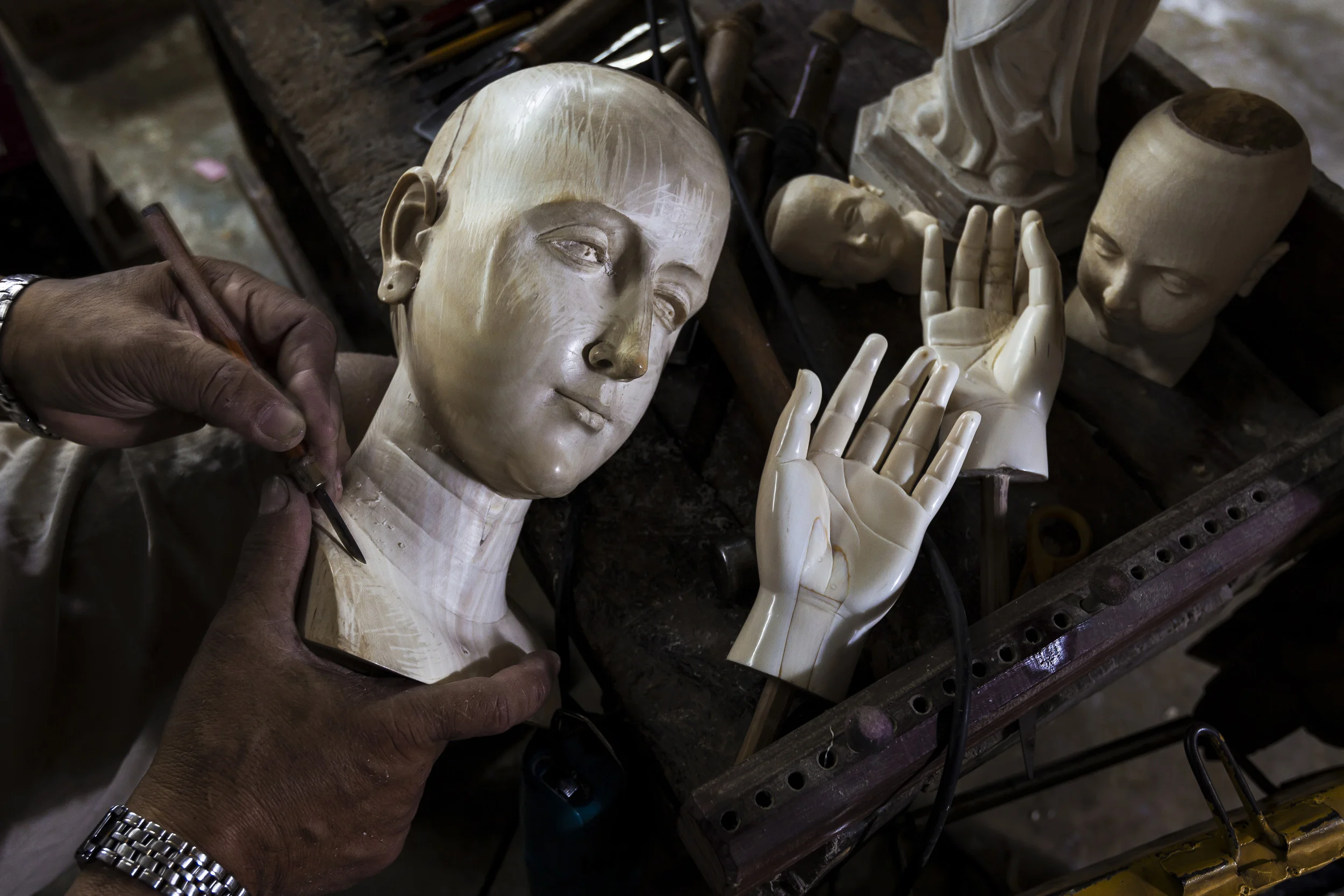 VALENZULEA, PHILIPPINES, JANUARY 2012: Master sculptor Marcial Bernales carves an Ivory head and hand set for a Catholic religious icon in his worshop in Valenzulea, close to Manila, Philippines, 25 January 2012. Bernales has been carving Ivory for 45 years and has made hundreds of pieces, all of which are of a religious nature in the Catholic faith in the Philippines. Many of these pieces are made with Ivory. His work is in the collections of many devotees and his ivory pieces are in great demand amongst the wealthy collectors of the Philippines. His workshop and workload are co-run by his wife Nene, who also runs his shop in Manila. She is a long running expert in the garments that clothe these religious icons. Their brisk trade is evidence of the demand for Ivory, they claims to use only pre-ban ivory but that is questionable given the attraction of price for ivory at 20000 pesos ($500) a kilo for raw ivory and far more for carved Benales masterpieces. It also illustrates the loophole in Ivory legislation whereby it is very difficult to tell pre-ban and post ban ivory apart. Once it is in the Philippines there are no records or statistics through which to verify claims, despite the fact that this is a centre for world ivory carving. (photo by Brent Stirton/Reportage for National Geographic Magazine.)