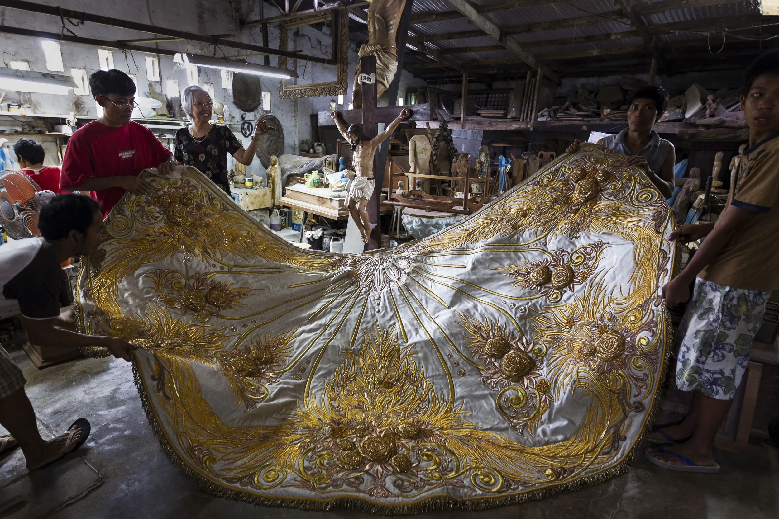 VALENZULEA, PHILIPPINES, JANUARY 2012: Master seamstress Nene Bernale displays a large cloak embroidered for a large Catholic religious icon in the worshop in Valenzulea, close to Manila, Philippines, 25 January 2012. Nene's husband Marcial Bernales has been carving Ivory for 45 years and has made hundreds of pieces, all of which are of a religious nature in the Catholic faith in the Philippines. Many of these pieces are made with Ivory. His work is in the collections of many devotees and his ivory pieces are in great demand amongst the wealthy collectors of the Philippines. His workshop and workload are co-run by his wife Nene, who also runs his shop in Manila. She is a long running expert in the garments that clothe these religious icons. Their brisk trade is evidence of the demand for Ivory, they claims to use only pre-ban ivory but that is questionable given the attraction of price for ivory at 20000 pesos ($500) a kilo for raw ivory and far more for carved Benales masterpieces. It also illustrates the loophole in Ivory legislation whereby it is very difficult to tell pre-ban and post ban ivory apart. Once it is in the Philippines there are no records or statistics through which to verify claims, despite the fact that this is a centre for world ivory carving. (photo by Brent Stirton/Reportage for National Geographic Magazine.)