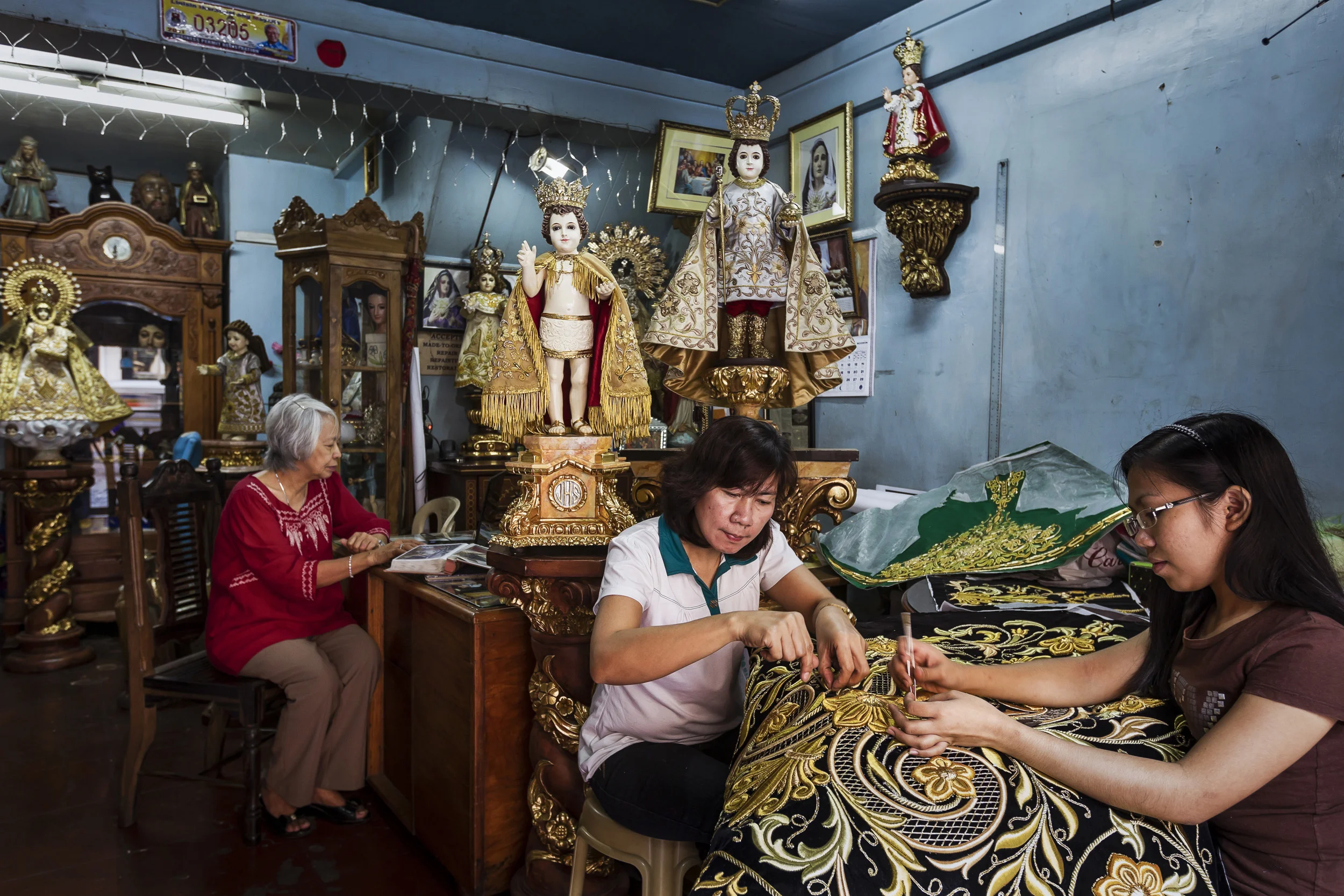 MANILA, PHILIPPINES, JANUARY 2012: Catholic icon dealer Nene Bernales and embroidery staff at work in her shop in Manila, Philippines, 25 January 2012. They are surrounded by Icons that have heads and hands made of Ivory. Nene's husband Marcial Bernales has been carving Ivory for 45 years and has made hundreds of pieces, all of which are of a religious nature in the Catholic faith in the Philippines. His work is in the collections of many devotees and his ivory pieces are in great demand amongst the wealthy collectors of the Philippines. His workshop and store are co-run by his wife Nene. She is a long time expert in the garments that clothe these religious icons. The brisk trade and high demand for Ivory icons is evidence of the demand for Ivory, the Bernale's claim to use only pre-ban ivory but that is questionable given the attraction of the very high prices paid for carved Benales masterpieces. There is not sufficent pre-ban supply to fullfill demand for these pieces in the Philippines. The Icon trade also further illuminates the loophole in Ivory legislation whereby it is very difficult to tell pre-ban and post ban ivory apart. Once raw ivory tusks are in the Philippines, there are no records or statistics through which to verify claims of legal ownership or criminality, despite the fact that this is a centre for world ivory carving. (photo by Brent Stirton/Reportage for National Geographic Magazine.)