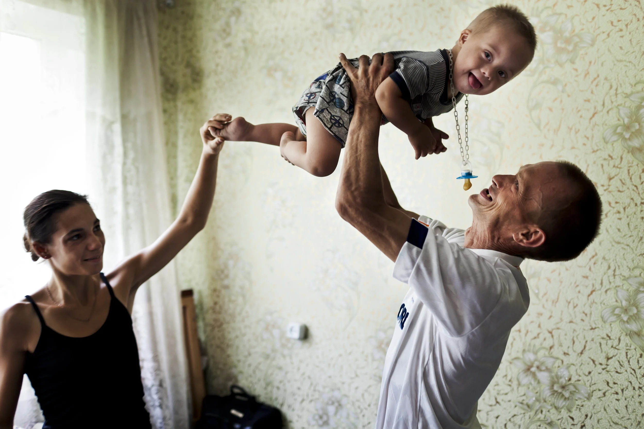 KRYVYI RIG, UKRAINE, AUGUST 2011: A very sick man living with full blown Aids holds up his young son while his wife looks on, Kryvyi Rig, Ukraine, 31 August 2011. This man has a very low T cell count and is almost certain to die soon. He recently married his girlfriend and the mother of his child to ensure she will inherit his possesions when he dies. The reason his case is so dire is because there have been no new admissions allowed to the list of Anti Retro-Viral therapy recipients for those people living with full blown Aids in Ukraine since the end of 2010. Nine months later in September 2011 all those people who have become critically ill but are not on the old list of ART recipients are living under a death sentence as their immune systems collapse. There is a new Government in Ukraine and the Ministry of Health controls all ART (Anti-RetroViral treatment,) medicine. As this business is put out to tender to the various pharmaceutical companies, a series of ignorances, bribes and corrupt practises hinder this vital service from coming into being in time to provide life-saving ART therapy to those who are dying without it. (Photo by Brent Stirton/Reportage for Getty Images.)