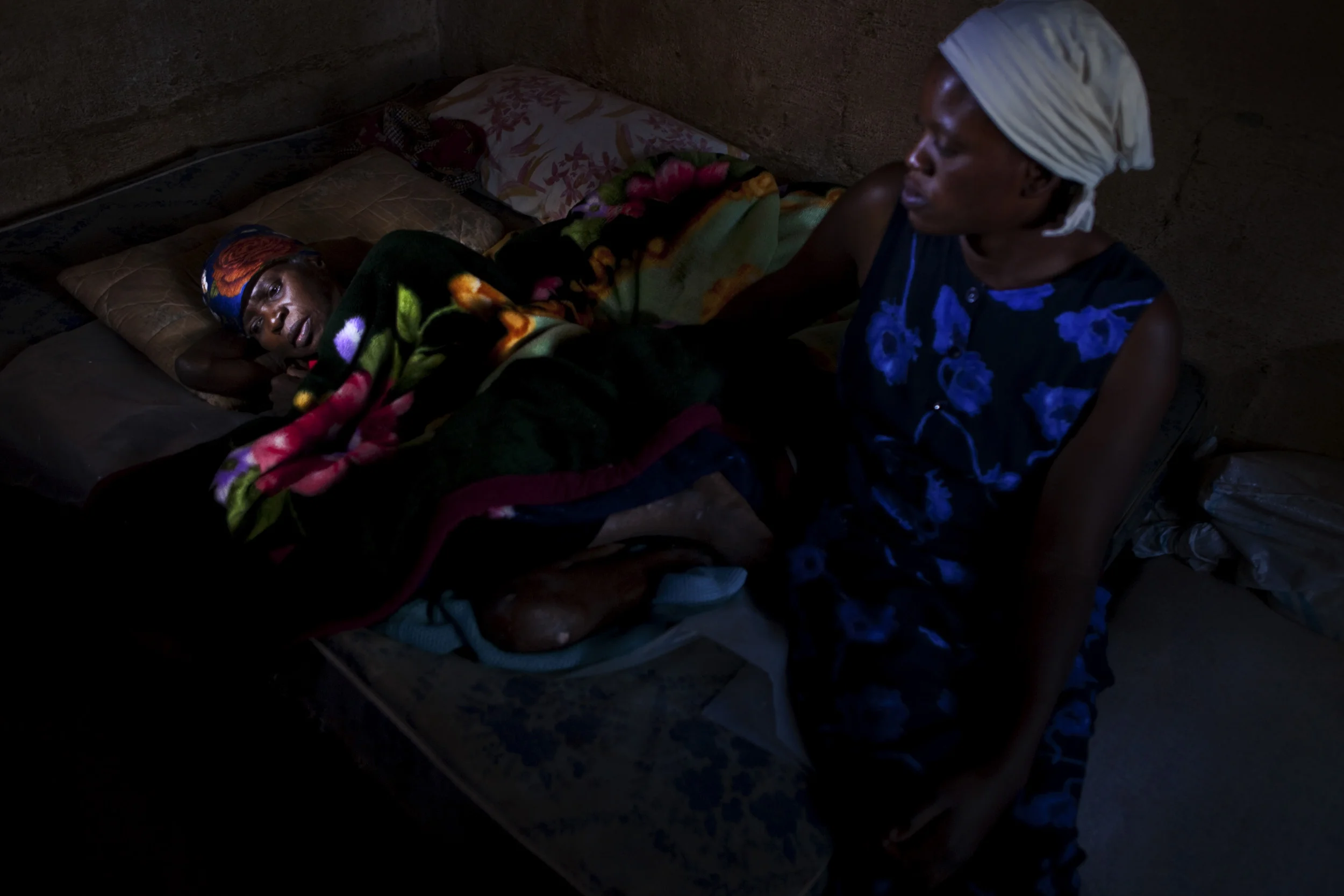 HARARE, ZIMBABWE, JUNE 2009: A daughter looks on at her HIV+ mother lying desperately ill in a one bedroom shack in a makeshift township in Harare, Zimbabwe, 21 June 2009. Neither are employed or have any money and they were turned away from the hospital for lack of fees for admission. Zimbabwe has a reportedly 24% HIV positive population, one of the highest rates of infection in the world. The Zanu PF government has crippled the economy as well as interfered in Aid coming into the country. There are no real Aids education campaigns, hospitals are extremely expensive and 85% of the population is unemployed. This has meant that healthcare is distant dream for most Zimbabweans. A few institutions offer Anti-Retroviral treatments but it costs an average of $20 to get through the neccesary testing to get on the program. Transport costs alone to and from the hospital are beyond the means of most Zimbaweans in this failed state. As a result of scarcity food malnutrition plays a large role in the decline of HIV+ Zimbabweans, even those fortunate enough to be on ARV treatment. (Photo by Brent Stirton/Reportage by Getty Images.)