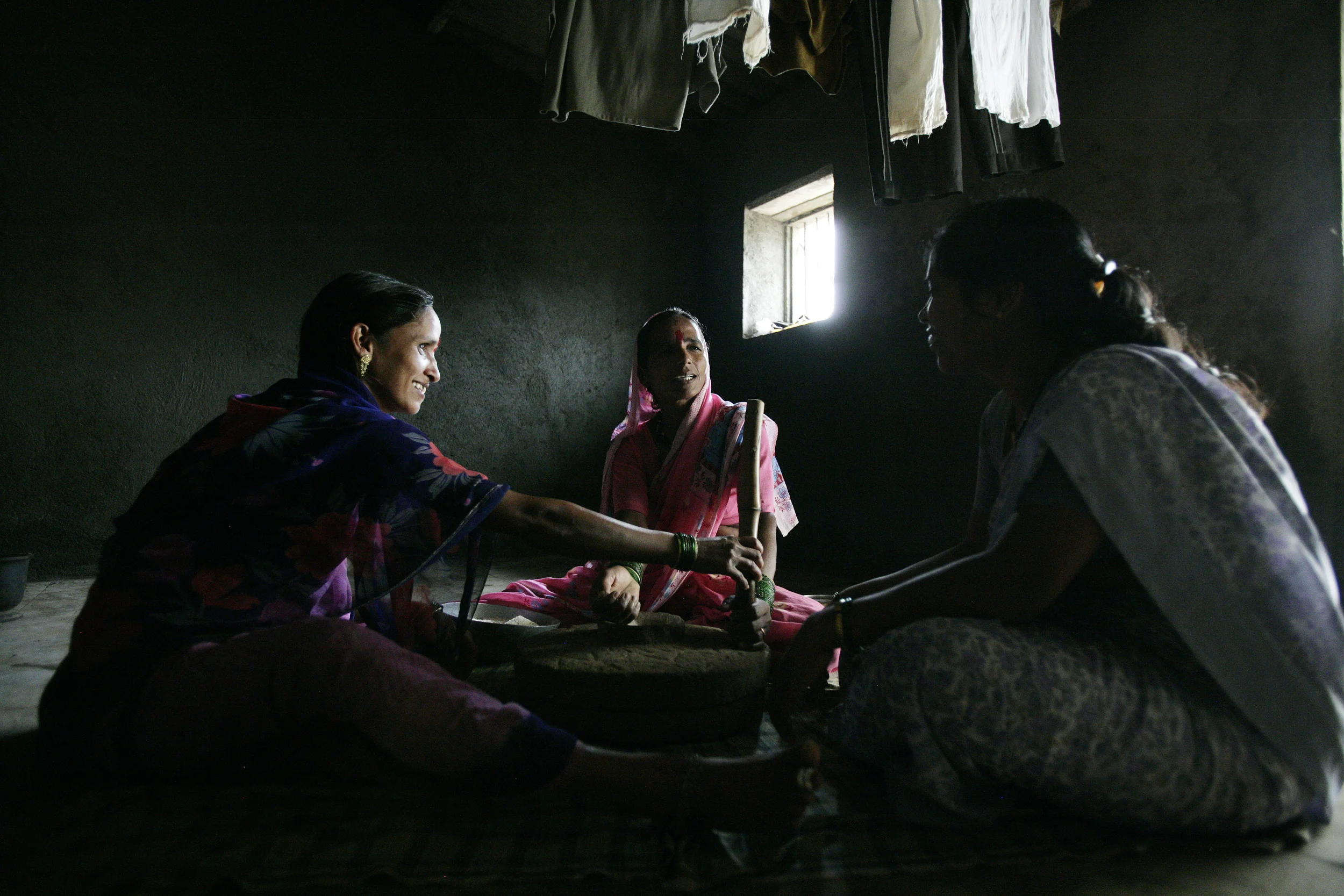 Pune, India, June 2006: Village women, one of which is HIV+, sit and grind corn while listening to a Peer counselor discuss HIV issues.