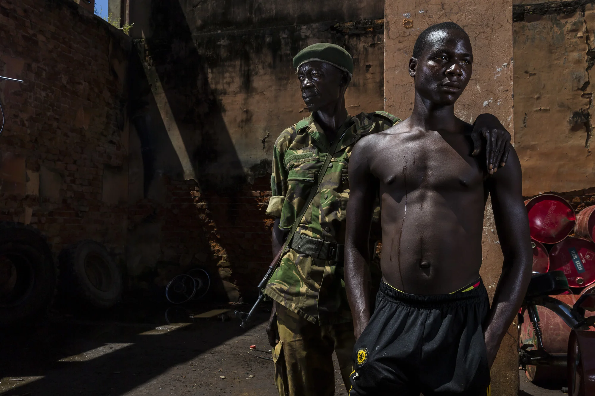 GARAMBA NATIONAL PARK, DEMOCRATIC REPUBLIC OF CONGO, 10 NOVEMBER 2014: Long time Africa Parks conservation Ranger Kumboyo Kobango Dieudo Onme, 62, is seen with his son Genekpio inside a damaged store room at the Park HQ for Garamba National Park. On 22 December 2008 Genekpio was abducted by notorious rebel group the Lord's Resistance Army, LRA, from his local village in Nagero, close to the Park. The LRA is notorious for these abductions, taking women and girls as cooks and sex slaves and young men and boys as porters and reinforcement fighters. The LRA took Genekpio and others and moved toward the Central African Republic, South Sudan border area. He saw the LRA attack another two villages in this time, killing multiple innocents and abducting 4 more children. He was also beaten on a daily basis and forced to watch the execution of other abductees as a lesson to the others not to try to escape. After 4 months, this LRA group was attacked by a force from the Ugandan Peoples Defence Force, UPDF. Genekpio was wounded 3 times in the leg in this attack but ultimately was rescued by the UPDF and returned to his family in Nagero. His Ranger father has had regular contacts with the LRA as they poach ivory in Garamba National Park and is still very angry about the abduction of his son. "It is better if they had taken me, I would have died to protect my son. Now I search for LRA on every patrol. If I see them they must die." This is an increasing issue for conservation's protectors as they find they are increasingly not only protecting wild areas and animal but also local populations for rebel groups acting with impunity in their areas. (Photo by Brent Stirton/Reportage by Getty Images for National Geographic Magazine.)