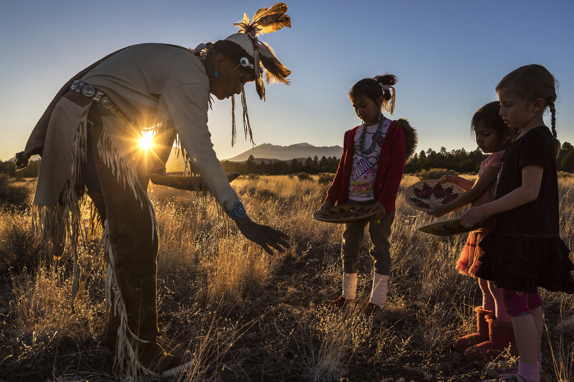FLAGSTAFF, ARIZONA, 7 APRIL 2014: Jones Benalli, a traditional medicine man of the Navajo tribe, seen with ceremonial bowls teaching his grand-daughters the secrets of traditional Navajo medicine, Flagstaff, Arizona, 7 April 2014. The bowls represent the heart of the Navajo spiritual world. Jones is seen with a sacred mountain behind him, a mountain that has been the center of a court case as a local ski lodge has been using recycled sewerage water to manufacture the snow which is spread over this sacred Navajo site. (Photo by Brent Stirton/Reportage for Figaro Magazine.)