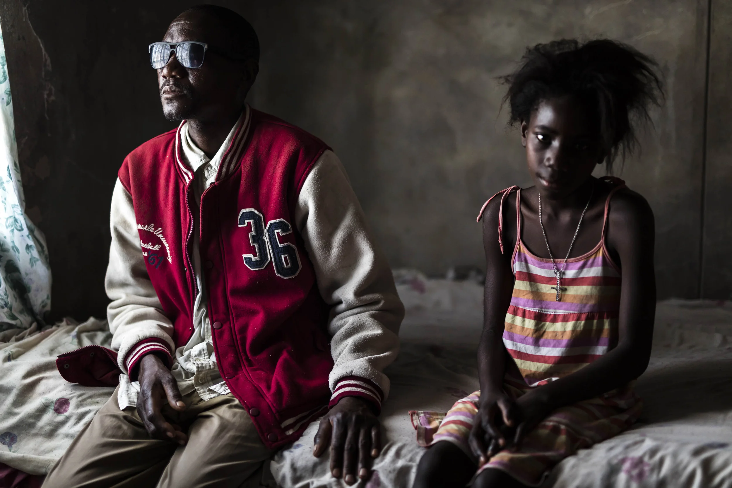 OHANGWENA DISTRICT, NORTHERN NAMIBIA, 8TH NOVEMBER 2015: Jason Hangula, 45, lost his sight in 2007 to a glucoma condition which was left untreated for too long. Damage to the optic nerve means that he is dependent on the children in his family compound for daily guidance to get around. He is seen with his niece Claudia Haindongo, 11, who has been assisting him ever since he lost his sight. For millions of people around the world blindness is something that affects entire families and communities. In the majority world children are often the caregivers of the blind. This can inhibit their education, their movement, their social circle and more. The majority of this is caused by blindness affecting the elderly; Glaucoma is common in many cases as is Corneal scarring and other issues affecting sight. Children most often function as a walking guide for these blinded people, helping them to get water, to bathe, to walk around and to fetch what is needed. Blindness in most instances is treatable if the issue is caught early enough. Access to quality eye care and education on the dangers are often lacking, hence the large incidence of blindness in the more remote regions of the world. (Photo by Brent Stirton/Reportage for National Geographic Magazine.)