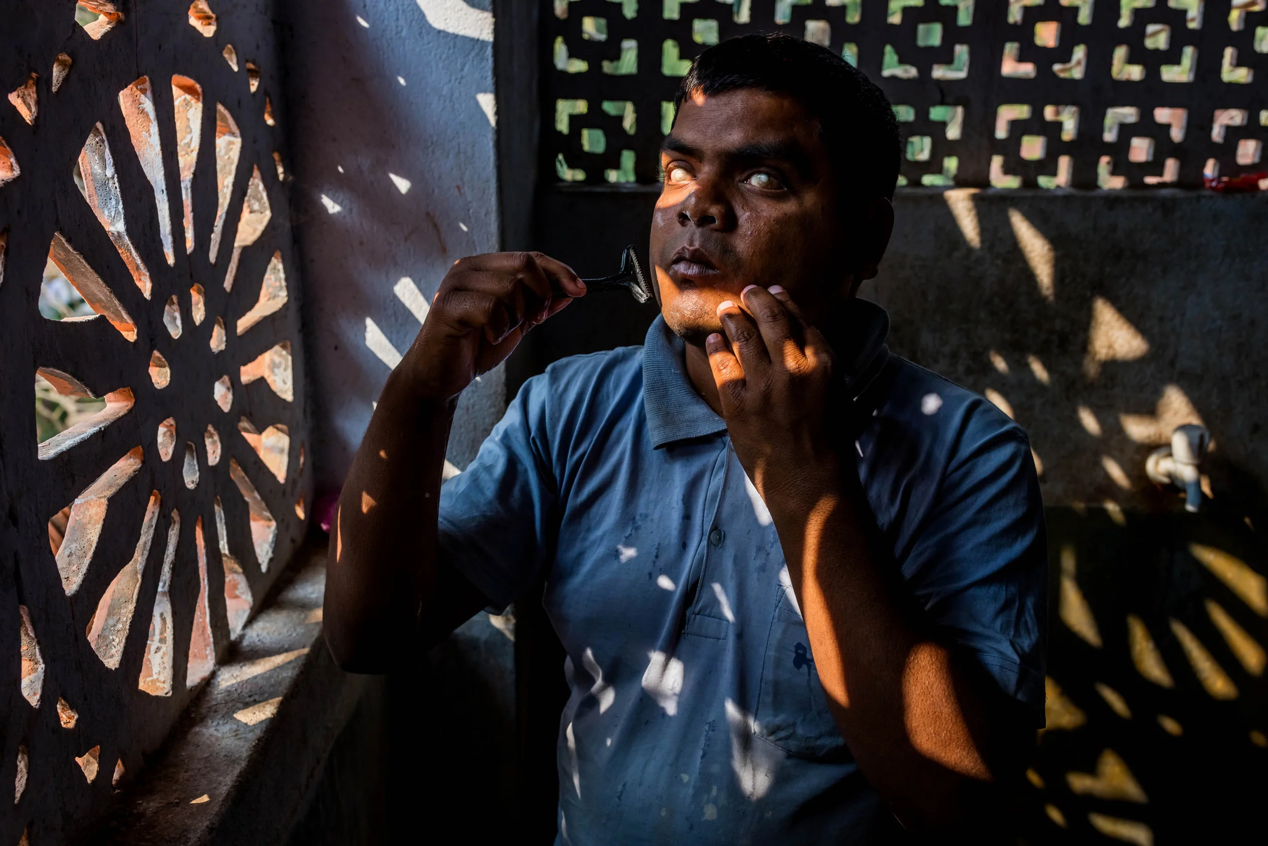 VIVEKANANDA MISSION ASRAM, HALDIA, WEST BENGAL, INDIA, JANUARY 14, 2016: A blind student shaves in dappled light in the bathroom in the hostel residence of the Vivekananda Mission Asram school for the blind. This is the highest rated school for blind children in India, the country with the highest number of blind people, arond 1% of their population, approximately 12 million people. Vivekanda Mission Asram provides care to some of the poorest of blind children, providing them with an education and tools for life survival once they leave the Asram after graduating. The children learn a normal school curiculum through braile and a team of dedicated teachers. Vocationa training is also available at the Asram in weaving, candle making amongst other skills that can add meaning to a blind life in India. Most of the blind in India end up as beggars, this school offers students a chance to be more than that. A number of their students have gone on to become senior teachers for sighted pupils, lawyers and business people. In these images the boys and girls are seen attending school lessons, learning Braille, music as well as scenes from their hostel residence and sports activities. (Photo by Brent Stirton/Reportage for National Geographic Magazine.)