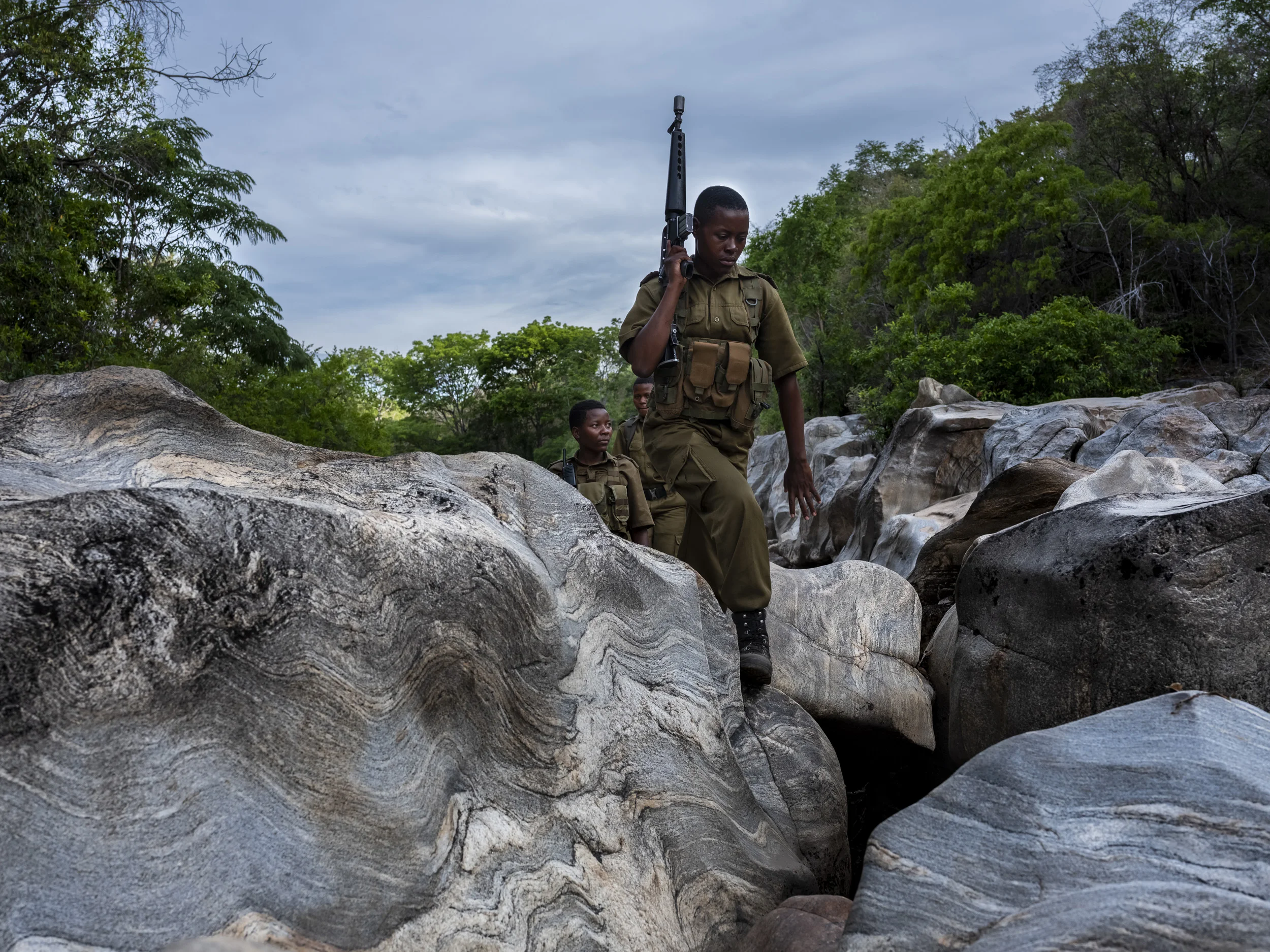 PHUNDUNDU WILDLIFE AREA, ZIMBABWE, DECEMBER 2018: A 5 member patrol walks through the wilderness they protect in Phundundu. This patrol is in the bush for 5 days at a time. They are part of an all female conservation ranger force known as “Akashinga” Akashinga (meaning the ‘Brave Ones’) is a community-driven conservation model, empowering disadvantaged women to restore and manage a network of wilderness areas as an alternative to trophy hunting in Zimbabwe. Predominately male forces are often hampered by ongoing corruption, nepotism, drunkenness, aggressiveness towards local communities and a sense of entitlement. The International Anti-Poaching Foundation, led by former Australian Special Forces soldier Damien Mander, was created as a direct action conservation organization used as a surgical instrument in targeting wildlife crime. In 2017 they decided to innovate, using an all- female team to manage an entire nature reserve in Zimbabwe. The program builds an alternative approach to the militarized paradigm of ‘fortress conservation’ that defends colonial boundaries between nature and humans. While still trained to deal with any situation they may face, the team has a community-driven interpersonal focus, working with rather than against the local population for the long-term benefits of their own communities and nature.