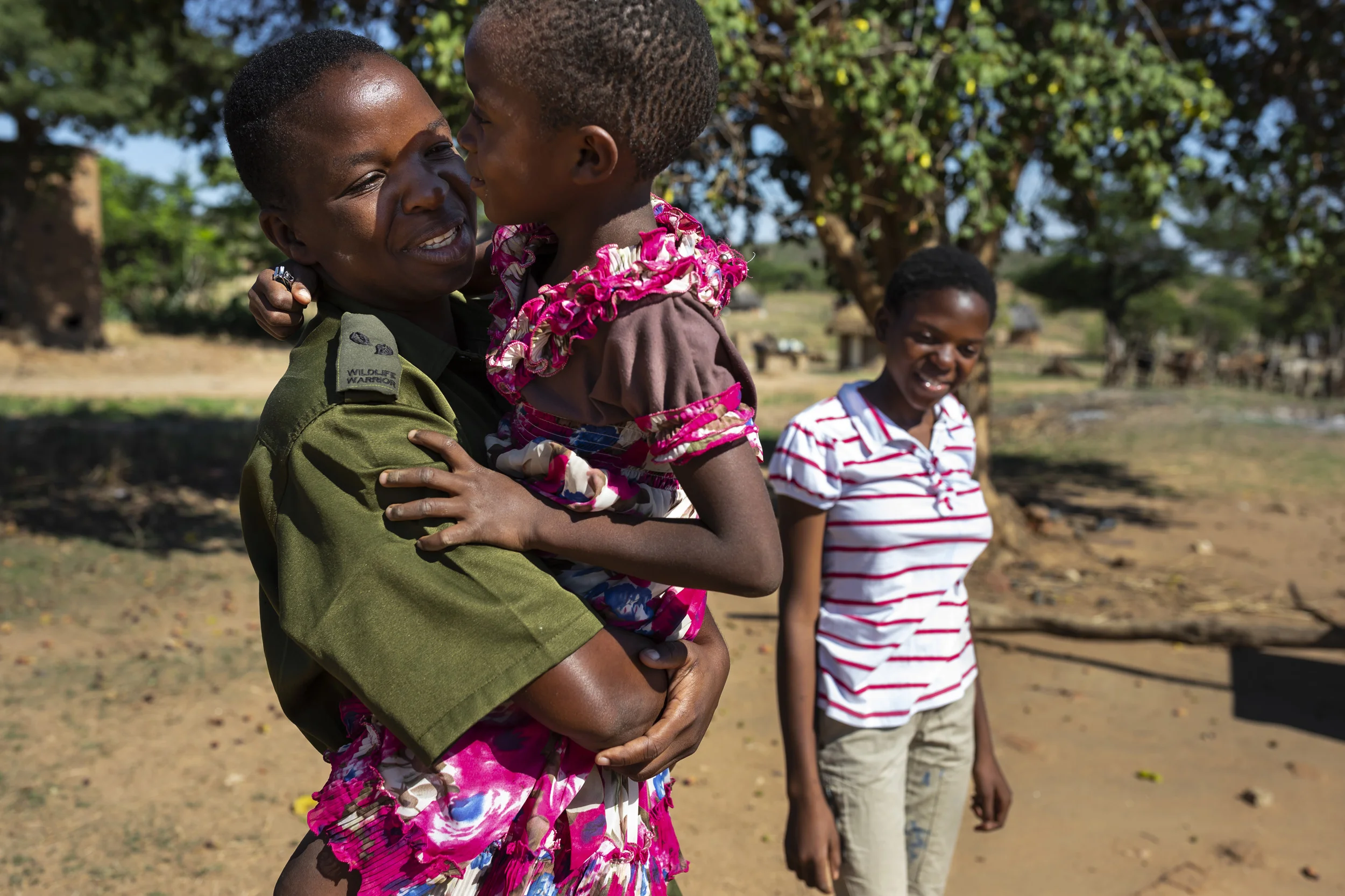 PHUNDUNDU WILDLIFE AREA, ZIMBABWE, DECEMBER 2018: Sergeant Vimbai Kamire comes home from the bush to visit her two daughters during her time off. Sergeant Vimbai is seen as a role model in her community. Through her conservation work she has distanced herself from an extremely abusive marriage and is now able to pay school fees for her children despite coming from the poorest demographic in Zimbabwe. She is part of an all female conservation ranger force known as “Akashinga” Akashinga (meaning the ‘Brave Ones’) is a community-driven conservation model, empowering disadvantaged women to restore and manage a network of wilderness areas as an alternative to trophy hunting in Zimbabwe. Predominately male forces are often hampered by ongoing corruption, nepotism, drunkenness, aggressiveness towards local communities and a sense of entitlement. The International Anti-Poaching Foundation, led by former Australian Special Forces soldier Damien Mander, was created as a direct action conservation organization used as a surgical instrument in targeting wildlife crime. In 2017 they decided to innovate, using an all- female team to manage an entire nature reserve in Zimbabwe. The program builds an alternative approach to the militarized paradigm of ‘fortress conservation’ that defends colonial boundaries between nature and humans. While still trained to deal with any situation they may face, the team has a community-driven interpersonal focus, working with rather than against the local population for the long-term benefits of their own communities and nature.