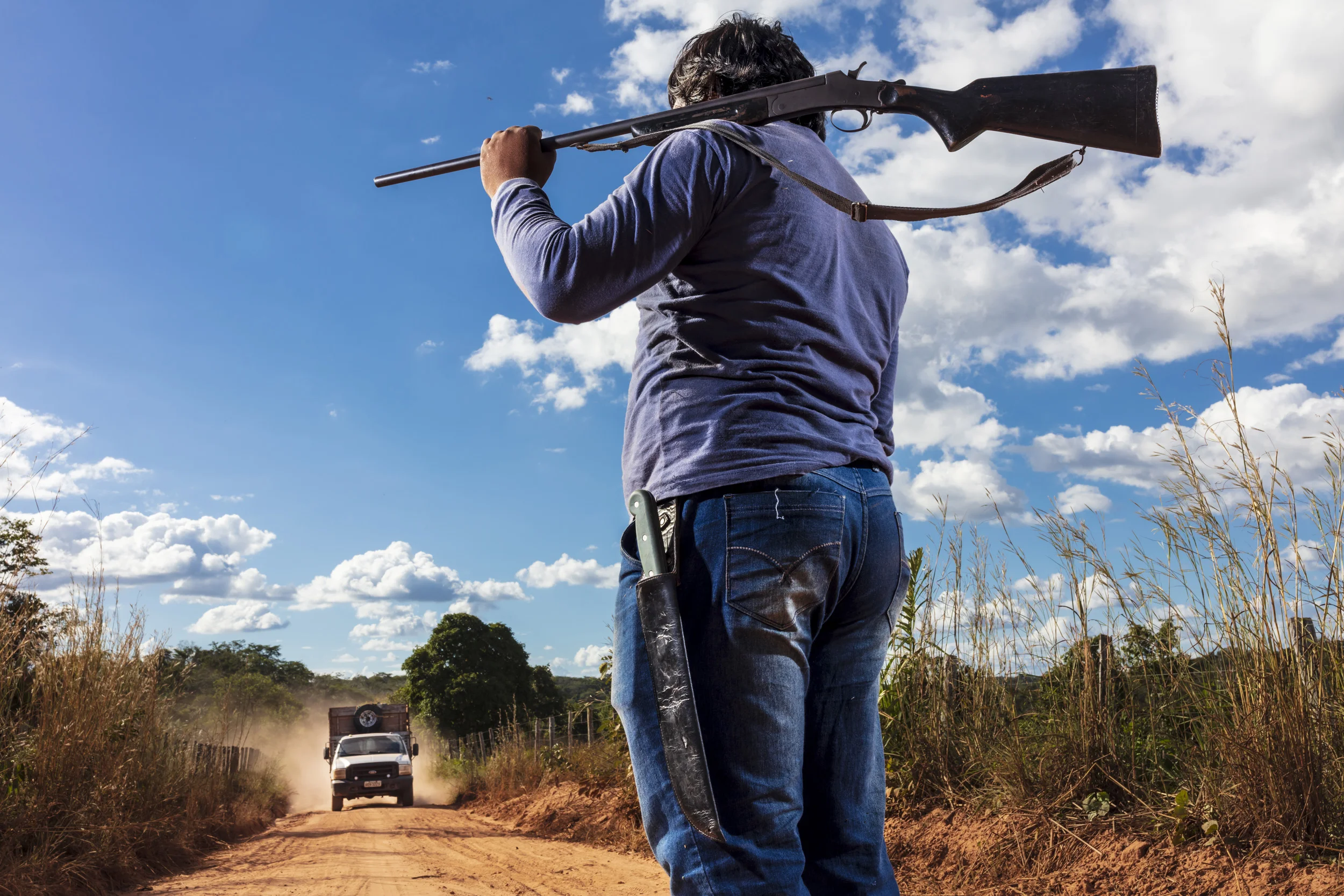 MARANHAO, BRAZIL, JUNE 2018: An illustration of a typical roadblock indigenlous people set up to look for illegal loggers on their land. This man is from the village of Governador, the central village in the tribal area for Gaviao Indigenous people. TI Governador is the ancestral territory of the Gavião people; it encompasses 42,000 hectares of Amazon forest. Governador has been noticeably affected by deforestation, with whole areas razed of trees, dry riverbeds and frequent forest fires. People in this village say that the old days were better, their forests held more animals for hunting, more fruit and there were no problems with loggers illegally cutting their timber.
This village was running a regular forest guardian patrol but funding for indigenous NGO’s has dried up and at this time there are no patrols due to that lack of funding. 3 years ago this village confiscated logging vehicles by force which led to a confrontation with the loggers. The village was abandoned by the military police, who were supposed to protect them from the illegal loggers. The military police only returned a week later during which time the village had to defend themselves. Environmental defenders in Governador have been subjected to threats, death threats, intimidation, assault and armed attacks. Defenders reported receiving threatening anonymous calls usually after seizing a truck during one of the patrols; sometimes the callers would also issue death threats towards the defender or towards their whole village. Loggers residing in the neighboring town have intimidated and physically assaulted at least 2 indigenous leaders when they traveled to town. In one instance loggers intimidated shop owners in town so they wouldn’t sell gas to indigenous people for two weeks. To date, there seem to have been no killings of Gavião environmental defenders in retaliation for their activism.
Gavião people are ambivalent about the role of the State. Several environmental defenders have work