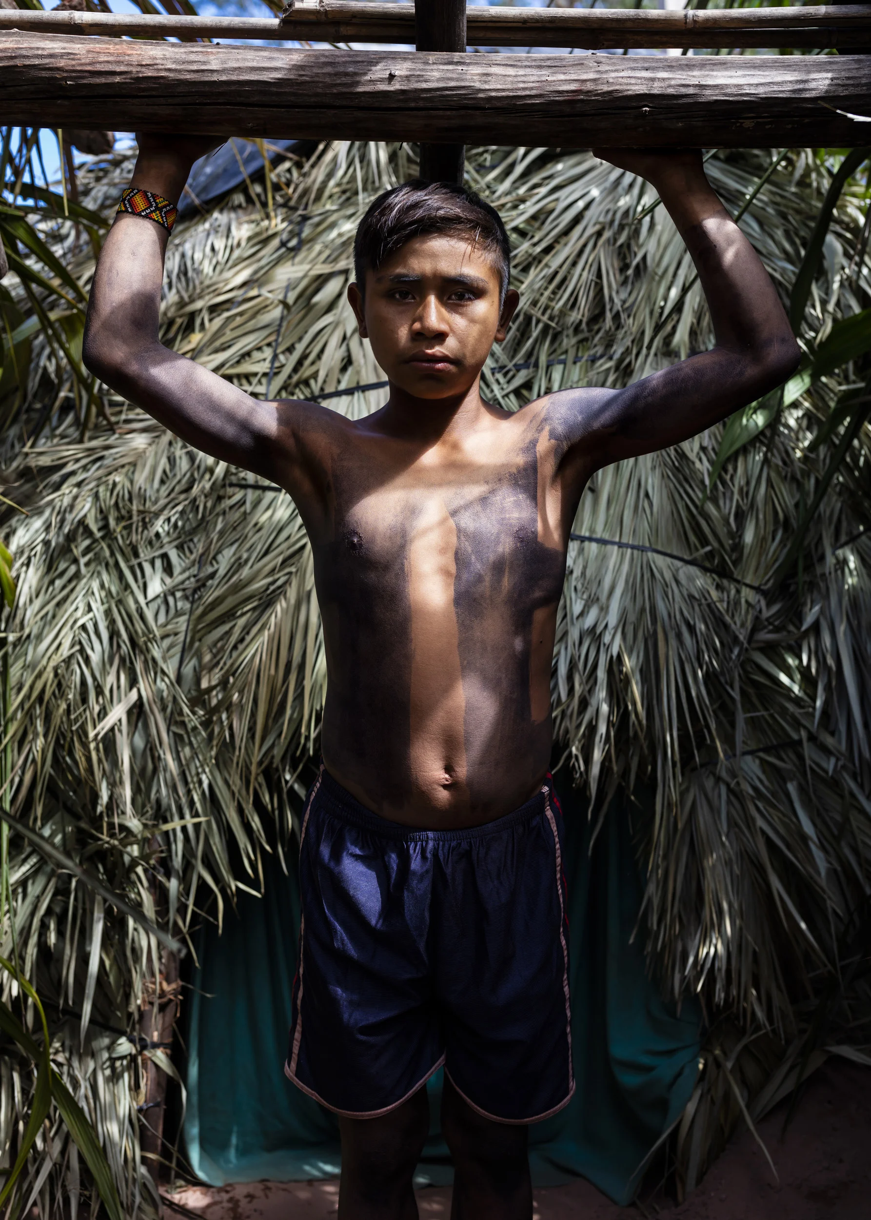 MARANHAO, BRAZIL, JUNE 2018: A young boy under- going a ritual month of isolation coming of age ceremony is seen in the village of Governador, the central village in the tribal area for Gaviao Indigenous people. TI Governador is the ancestral territory of the Gavião people; it encompasses 42,000 hectares of Amazon forest. Governador has been noticeably affected by deforestation, with whole areas razed of trees, dry riverbeds and frequent forest fires. People in this village say that the old days were better, their forests held more animals for hunting, more fruit and there were no problems with loggers illegally cutting their timber.
This village was running a regular forest guardian patrol but funding for indigenous NGO’s has dried up and at this time there are no patrols due to that lack of funding. 3 years ago this village confiscated logging vehicles by force which led to a confrontation with the loggers. The village was abandoned by the military police, who were supposed to protect them from the illegal loggers. The military police only returned a week later during which time the village had to defend themselves. Environmental defenders in Governador have been subjected to threats, death threats, intimidation, assault and armed attacks. Defenders reported receiving threatening anonymous calls usually after seizing a truck during one of the patrols; sometimes the callers would also issue death threats towards the defender or towards their whole village. Loggers residing in the neighboring town have intimidated and physically assaulted at least 2 indigenous leaders when they traveled to town. In one instance loggers intimidated shop owners in town so they wouldn’t sell gas to indigenous people for two weeks. To date, there seem to have been no killings of Gavião environmental defenders in retaliation for their activism.
Gavião people are ambivalent about the role of the State. Several environmental defenders have worked or continue to work with Funai, the