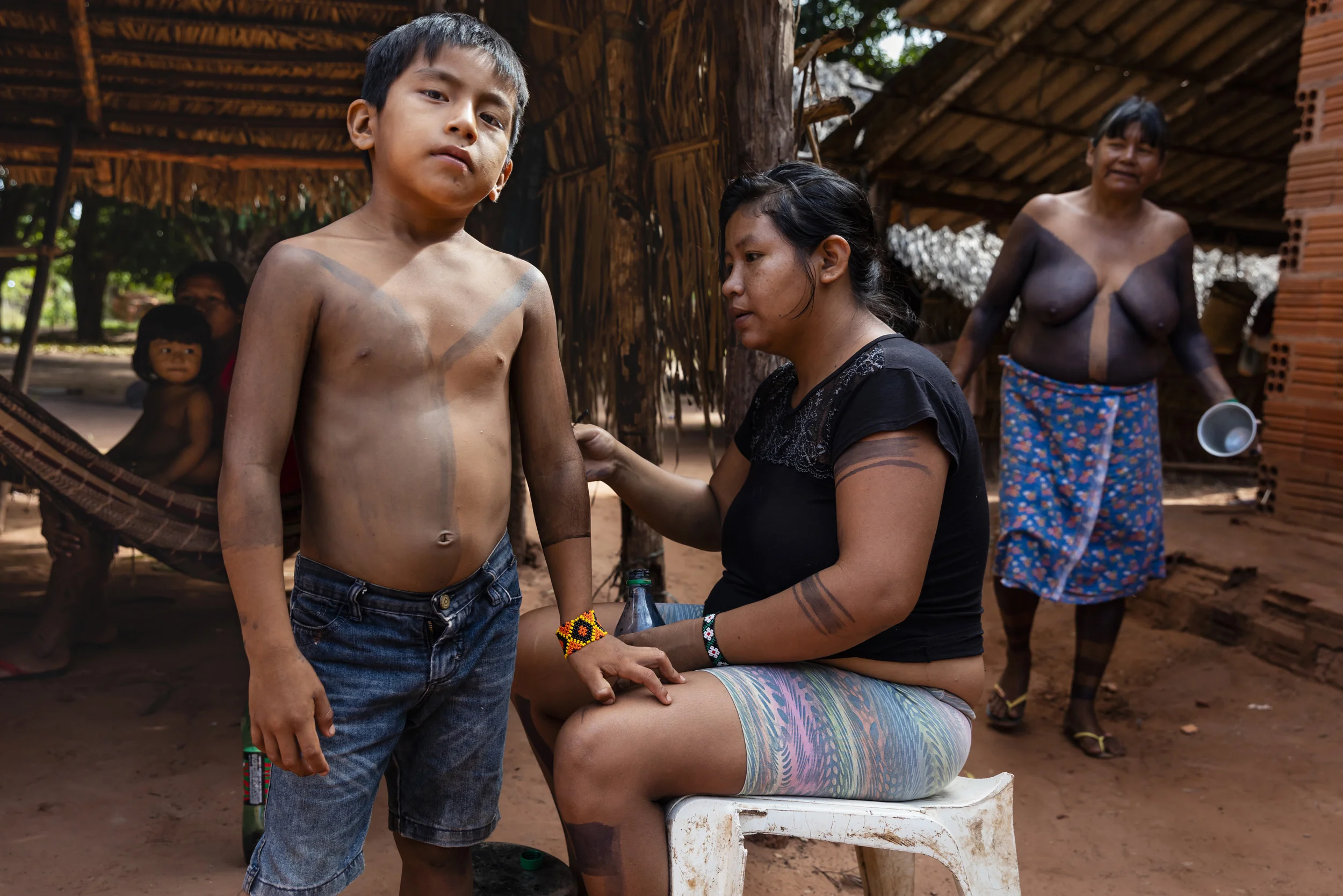 MARANHAO, BRAZIL, JUNE 2018: A yoing boy is painted wth tradional patterns in a scene from the village of Governador, the central village in the tribal area for Gaviao Indigenous people. TI Governador is the ancestral territory of the Gavião people; it encompasses 42,000 hectares of Amazon forest. Governador has been noticeably affected by deforestation, with whole areas razed of trees, dry riverbeds and frequent forest fires. People in this village say that the old days were better, their forests held more animals for hunting, more fruit and there were no problems with loggers illegally cutting their timber.
This village was running a regular forest guardian patrol but funding for indigenous NGO’s has dried up and at this time there are no patrols due to that lack of funding. 3 years ago this village confiscated logging vehicles by force which led to a confrontation with the loggers. The village was abandoned by the military police, who were supposed to protect them from the illegal loggers. The military police only returned a week later during which time the village had to defend themselves. Environmental defenders in Governador have been subjected to threats, death threats, intimidation, assault and armed attacks. Defenders reported receiving threatening anonymous calls usually after seizing a truck during one of the patrols; sometimes the callers would also issue death threats towards the defender or towards their whole village. Loggers residing in the neighboring town have intimidated and physically assaulted at least 2 indigenous leaders when they traveled to town. In one instance loggers intimidated shop owners in town so they wouldn’t sell gas to indigenous people for two weeks. To date, there seem to have been no killings of Gavião environmental defenders in retaliation for their activism.
Gavião people are ambivalent about the role of the State. Several environmental defenders have worked or continue to work with Funai, the specialised governmental