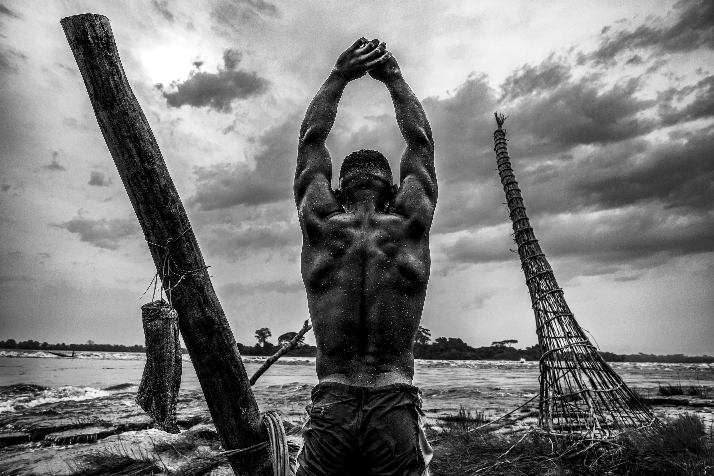 KISANGANI, DEMOCRATIC REPUBLIC OF CONGO: A portrait of a fisherman stretching before he lowers a large wicker fishing net into the rapids outside the city of Kisangani on the Congo River. Fisherman in this region are commonly affected by Onchocercia