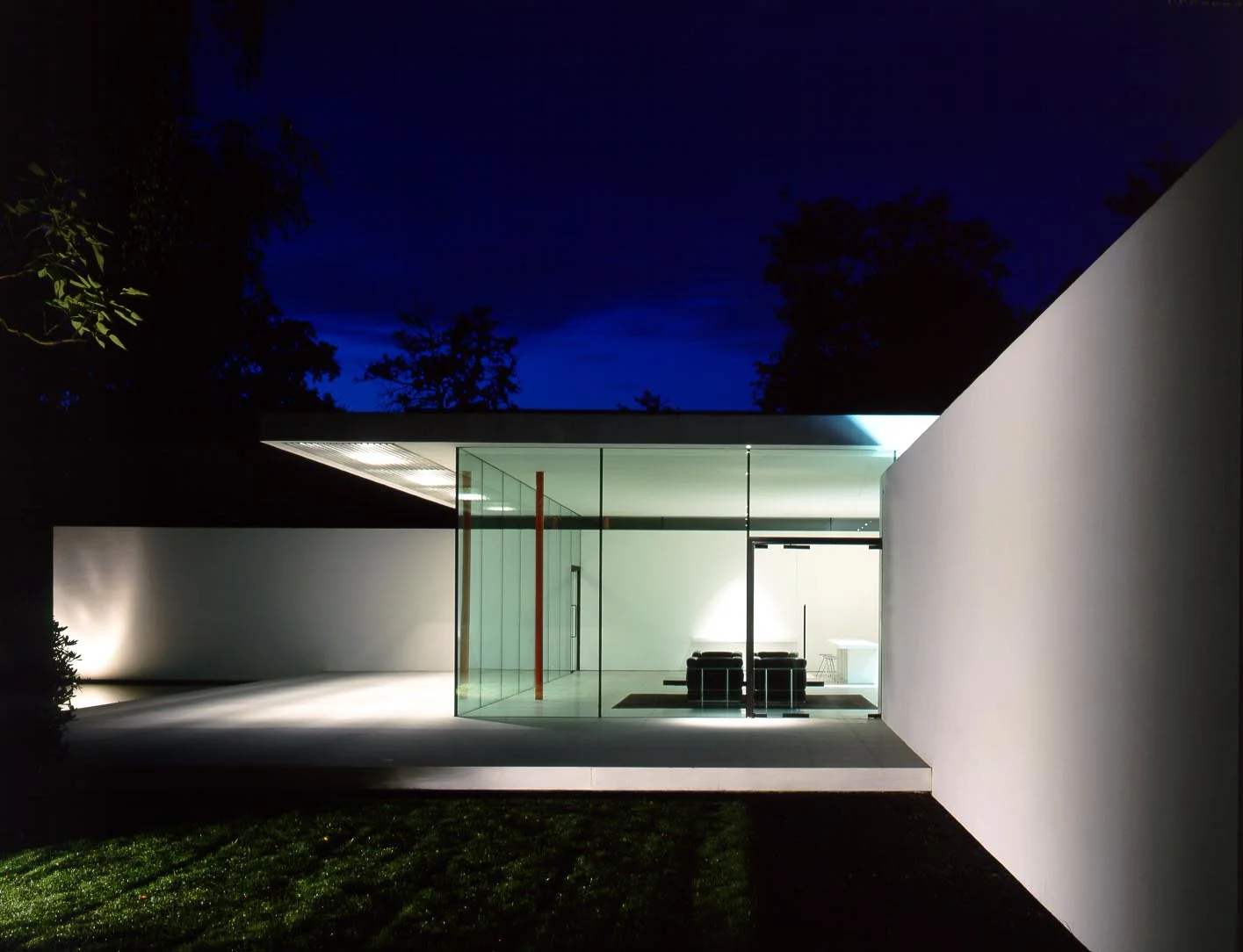 The floating roof plane is mirrored by the stone plinth base . Exterior lighting in the canopy and floodlights against the walls, including uplights in the water enhance the transparaency at night. 