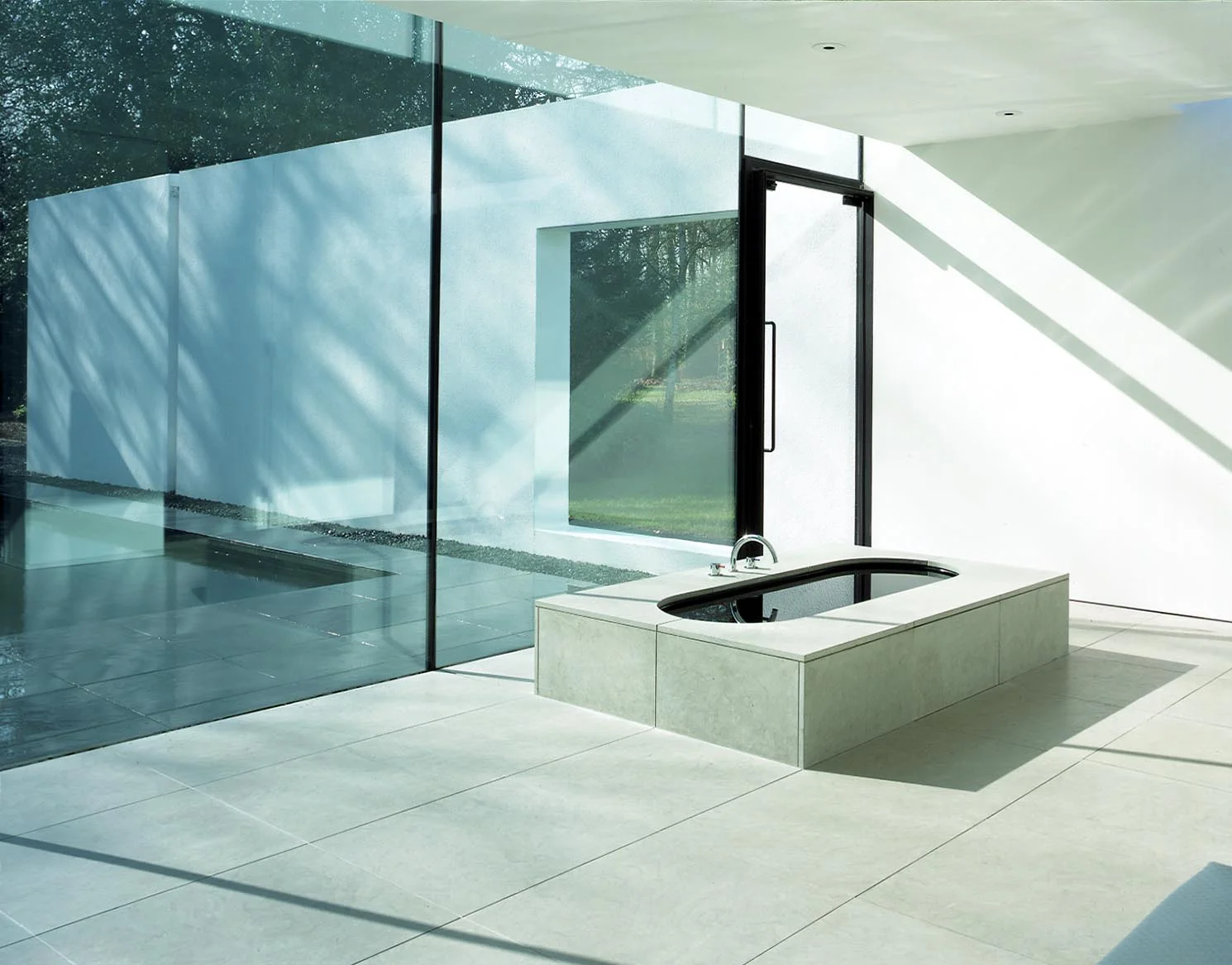 The bath in the master bedroom is open to the whole room with views into the walled garden. The black bath is filled with water and compliments the black reflecting swimming pool which it overlooks.
