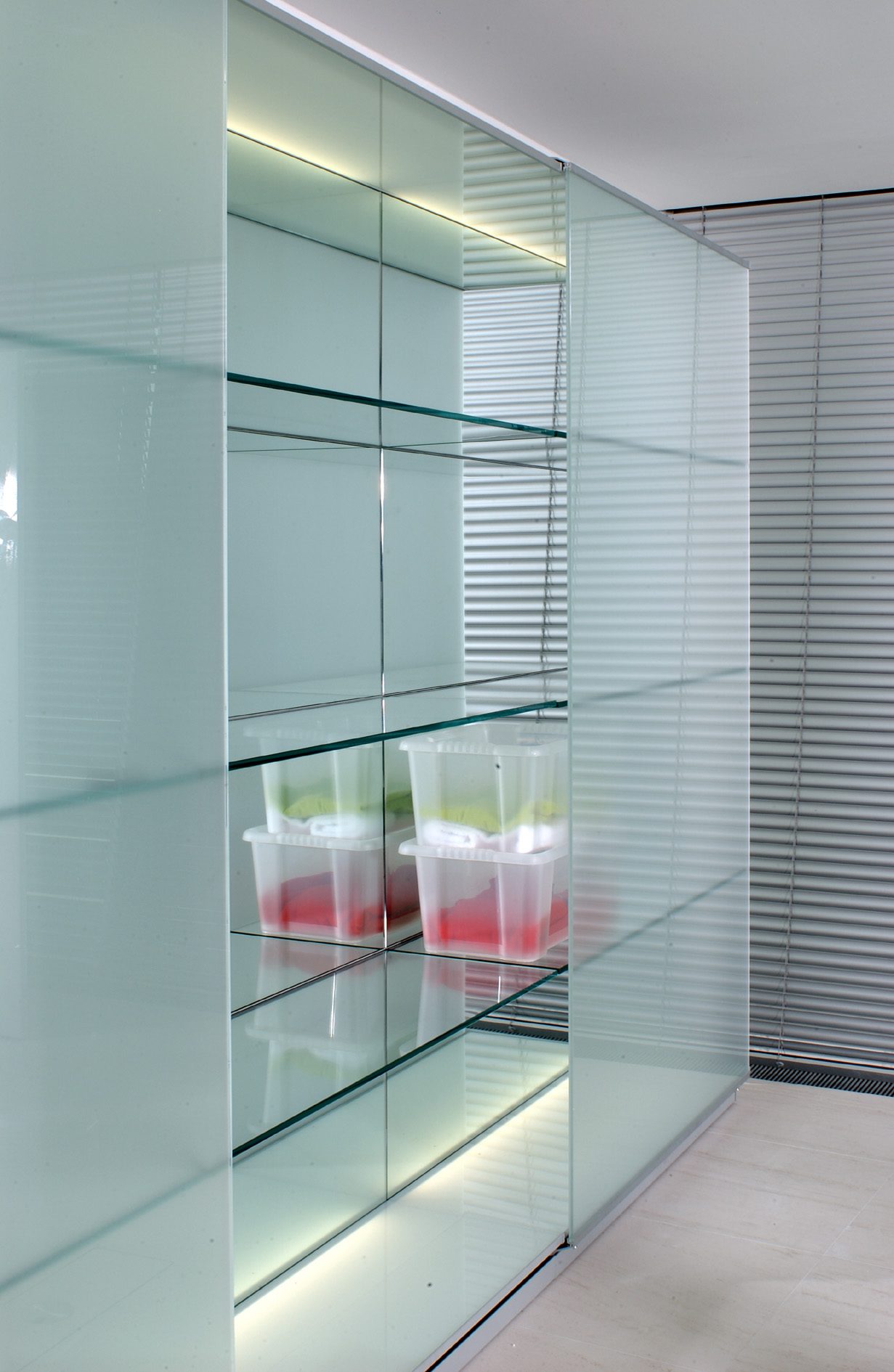 The custom designed storage display unit runs 11 m along the side wall. Sliding etched glass doors are on a 1.2 m module. Inside the glass shelves are cantilevered and have a mirror backing . There is dimmable concelaed lighting at the top and bottom of the unit.