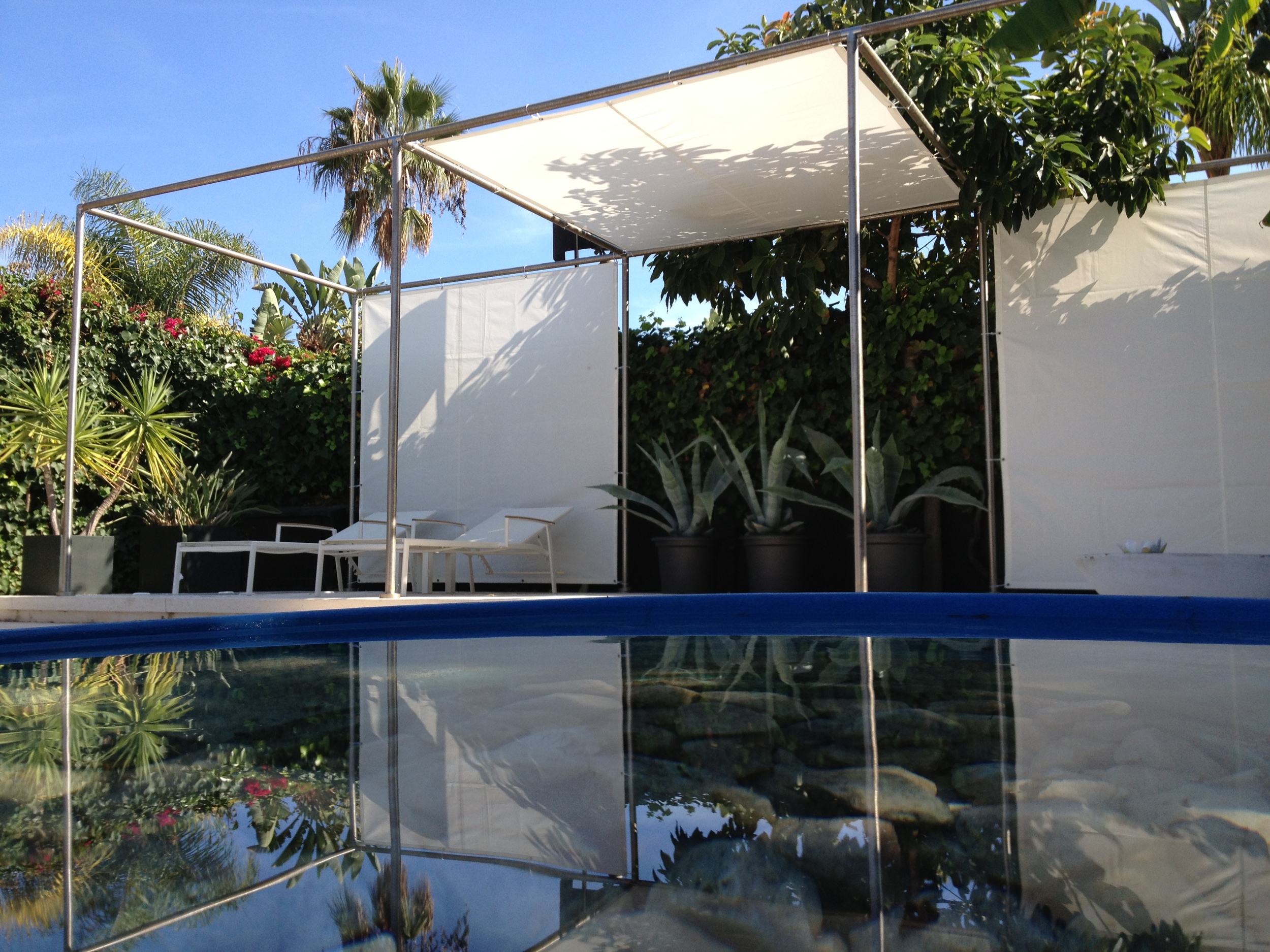 On the south side of the swimming pool there is a stainless steel structure of a 2.4 m module on a raised concrete plinth that has interchangeable white sailcloth panels to create shade as required.