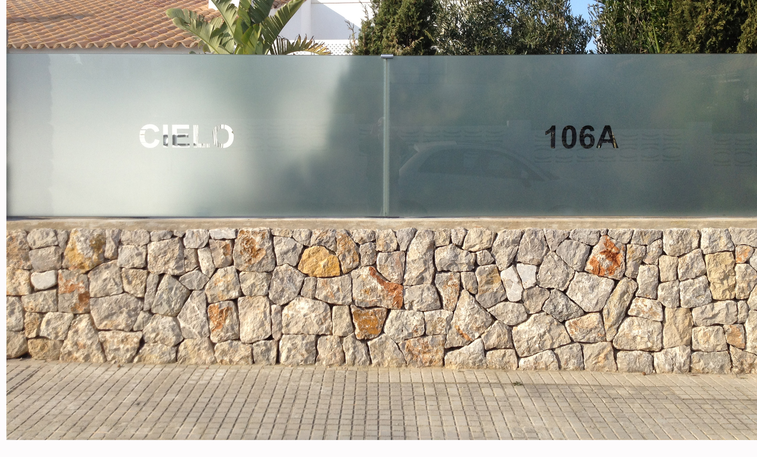 Original stone wall to the street retained but with the metal railings replaced with a frame less glass balustrsde . The name and number of the house are cut out of the translucent film.