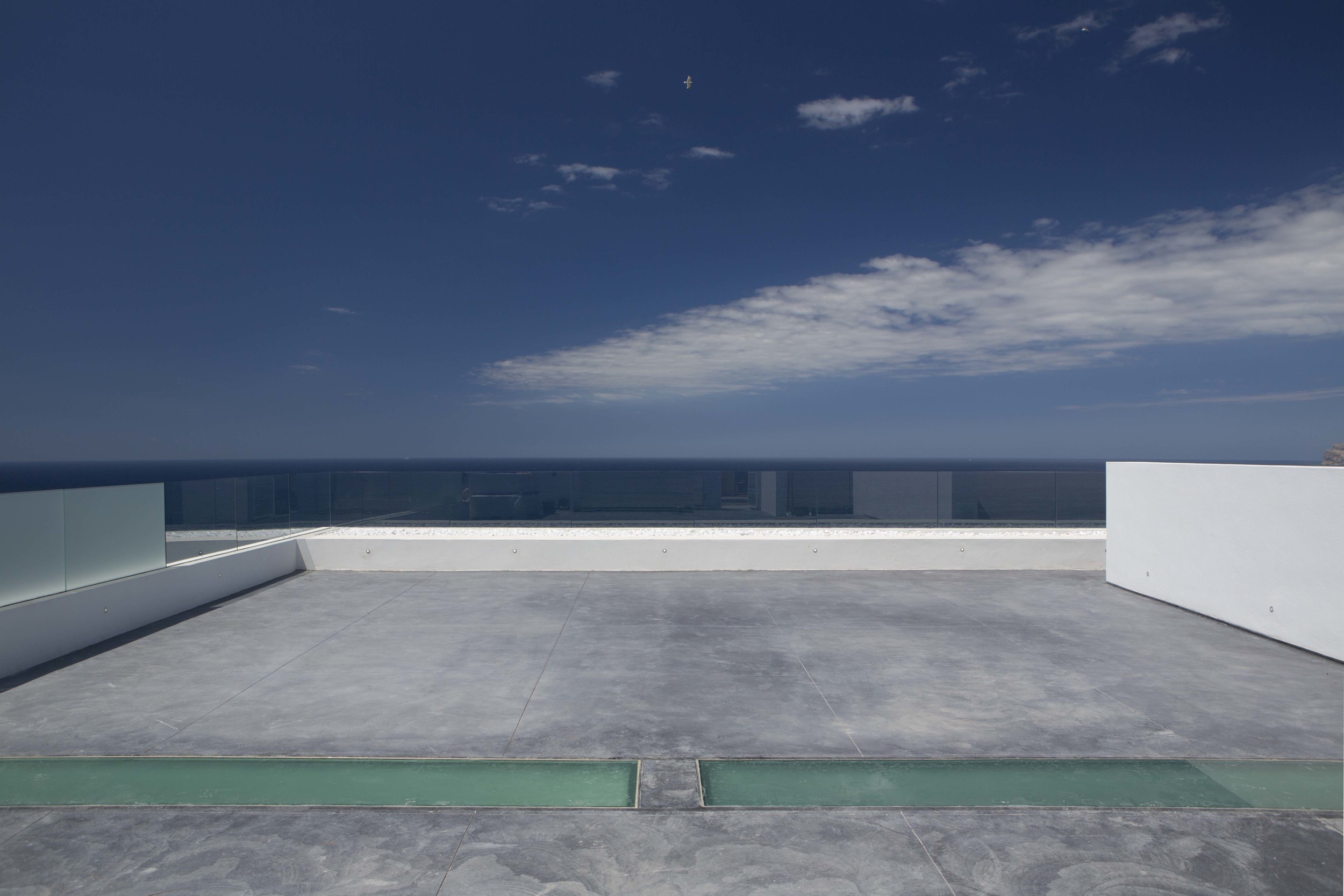 The street level roof space is used for parking . The concrete has a polished finish and is divided into large panels. The perimeter upstand is topped with a glass balustrade.