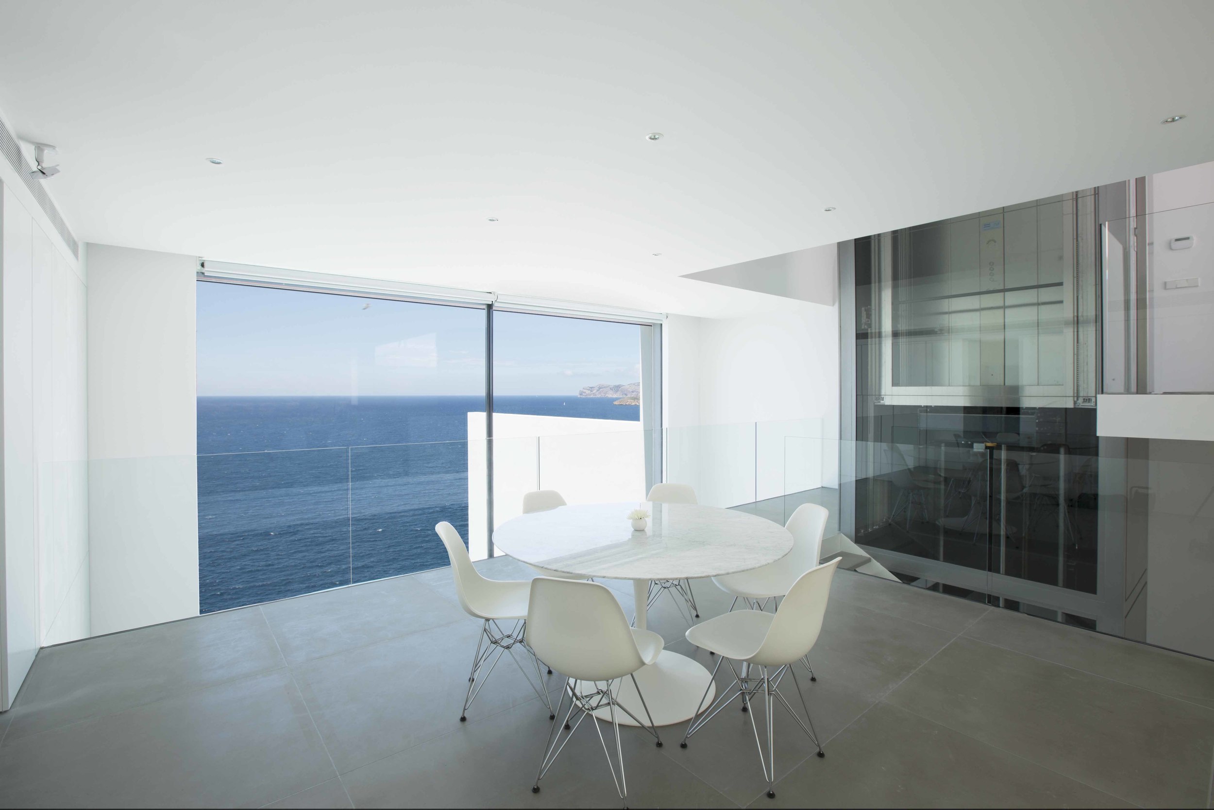 The mezzanine dining area is surrounded by a transparent glass balustrade with the glass lift structure to the right.