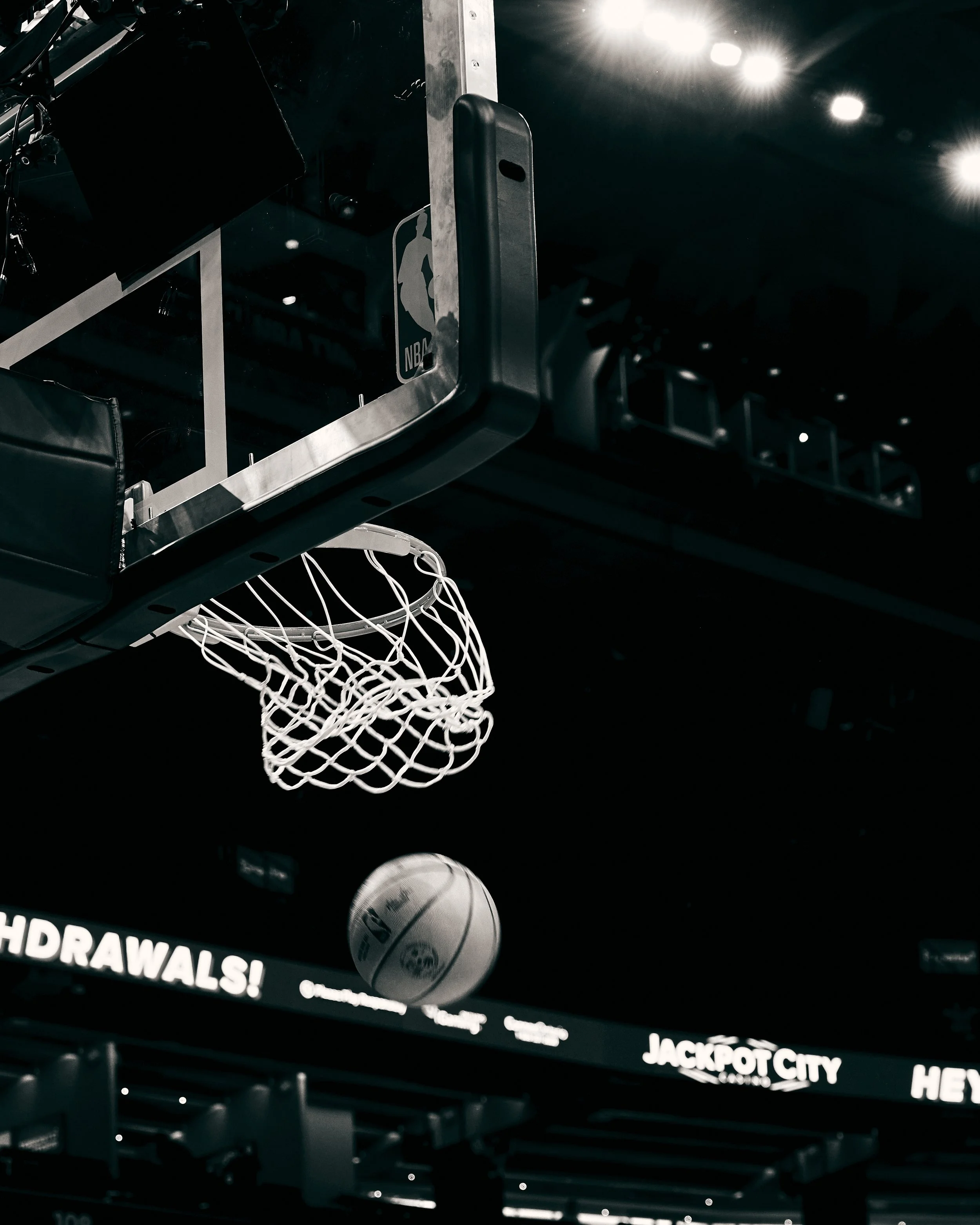 A basketball hoop with a white net hangs beneath a basketball rim. A basketball ball is visible in the background, and a digital display screen shows promotional text.