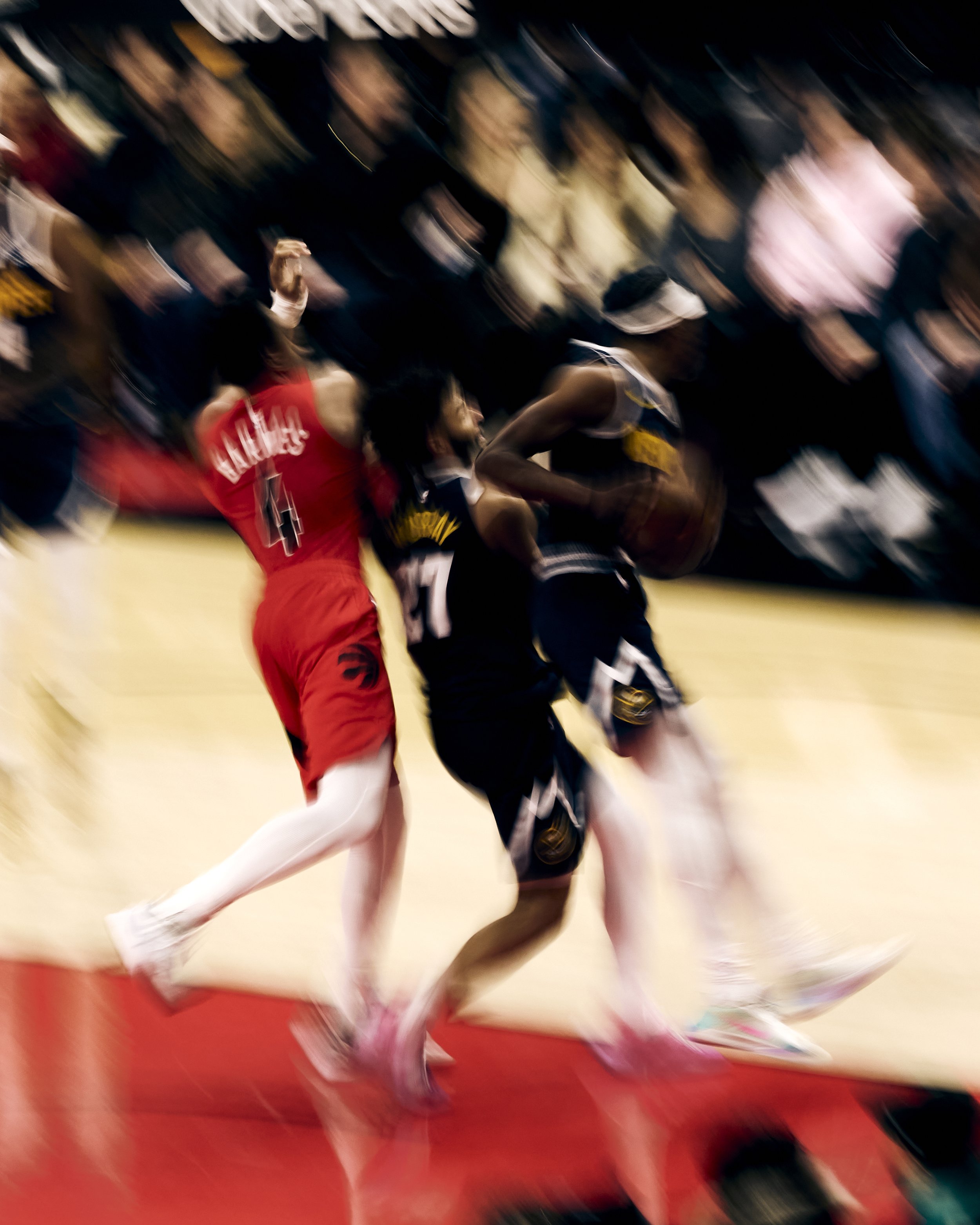 A group of basketball players in action during a game, with some players wearing red jerseys and others in black and gold jerseys, on a basketball court with a red floor.