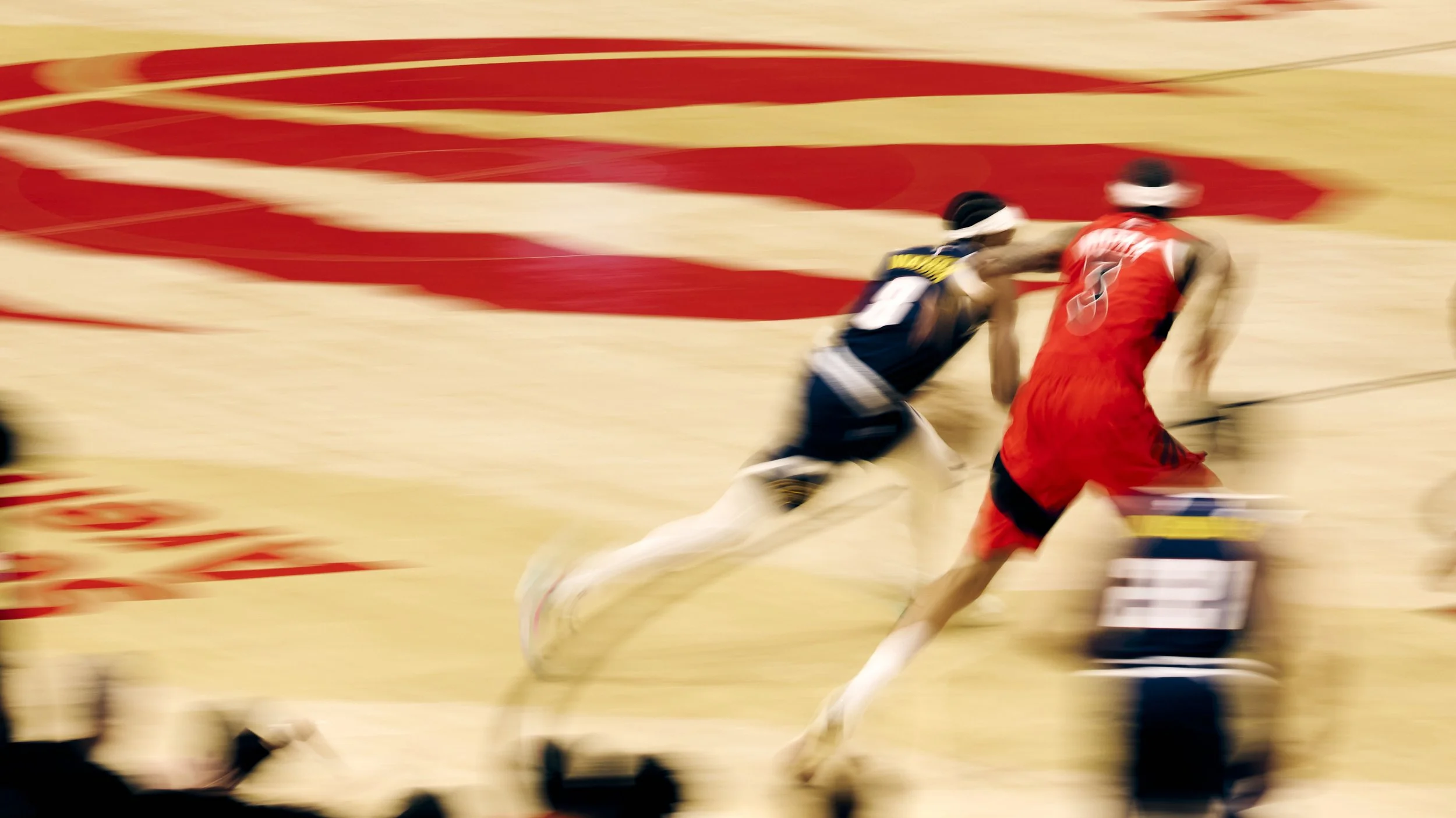Two sprinters competing in a race, wearing athletic gear and running on a track with blurred red and white markings.