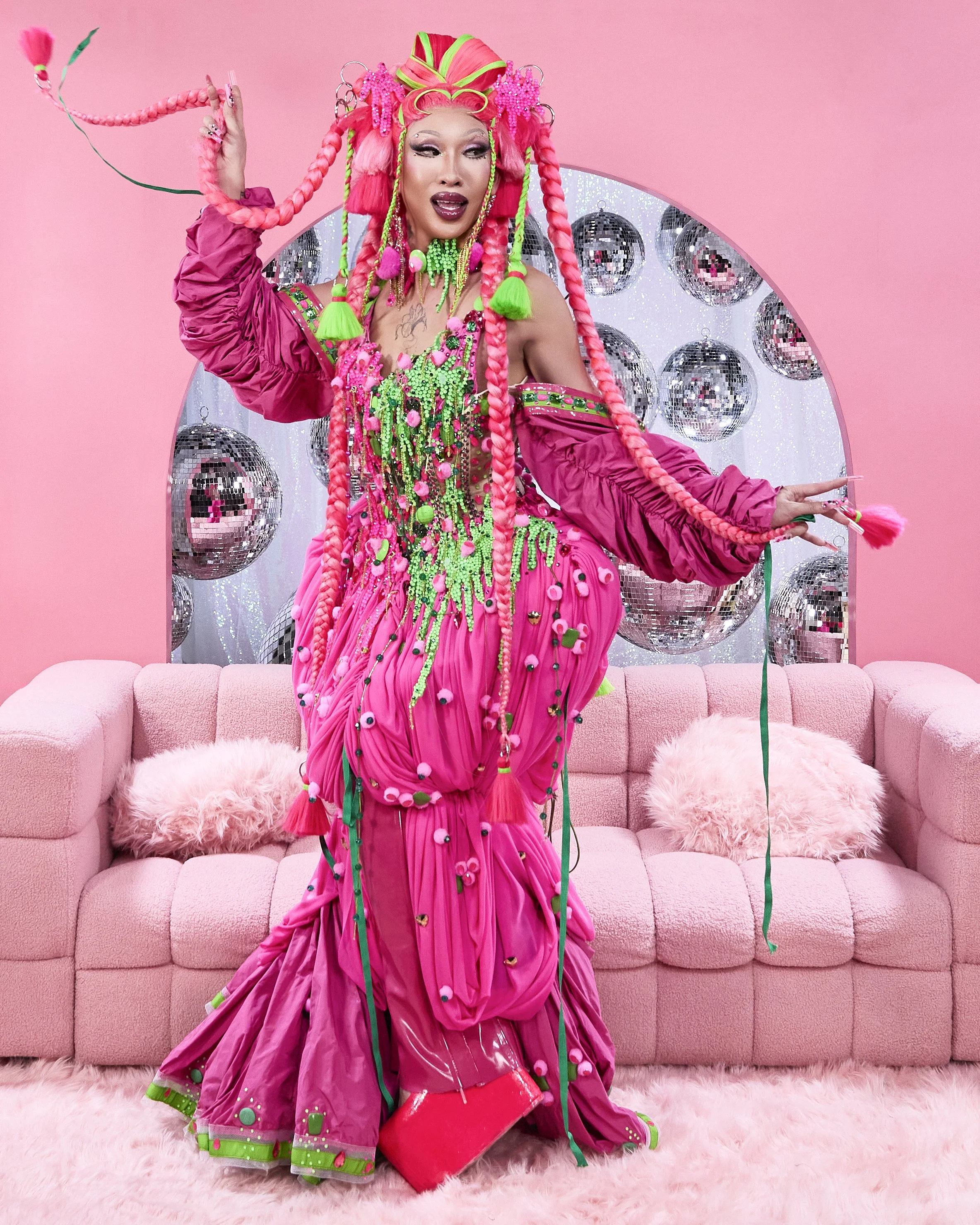 Suki Doll dressed in a vibrant, pink, green, and multicoloured costume with elaborate braids, jewelry, and accessories, on The Last Squeeze, Season 1.