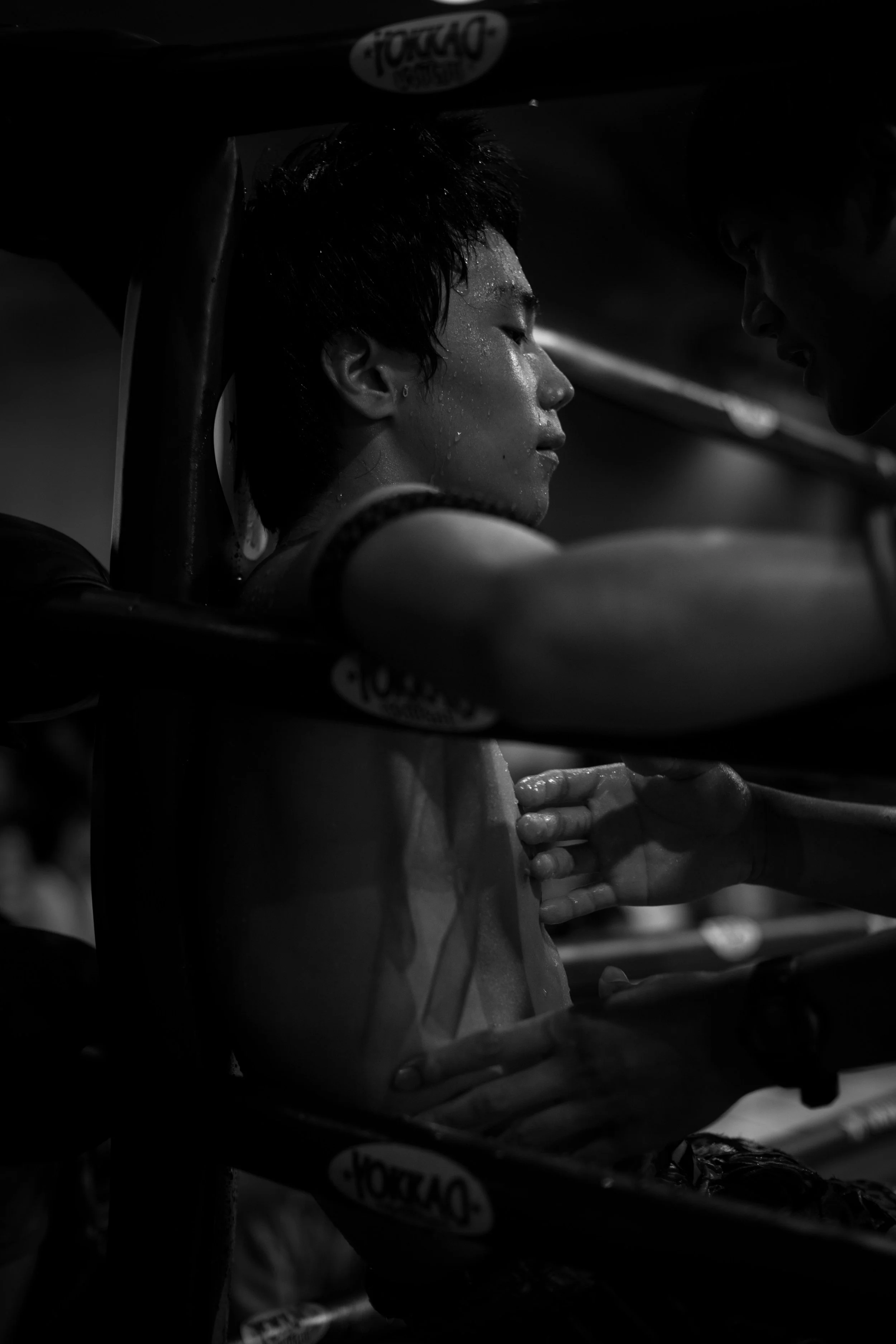 Thailand, Muay Thai A young person in a boxing gym, sweating and resting against the wall, while another person is touching their shoulder. Ring side during a Muay Thai match in Thailand