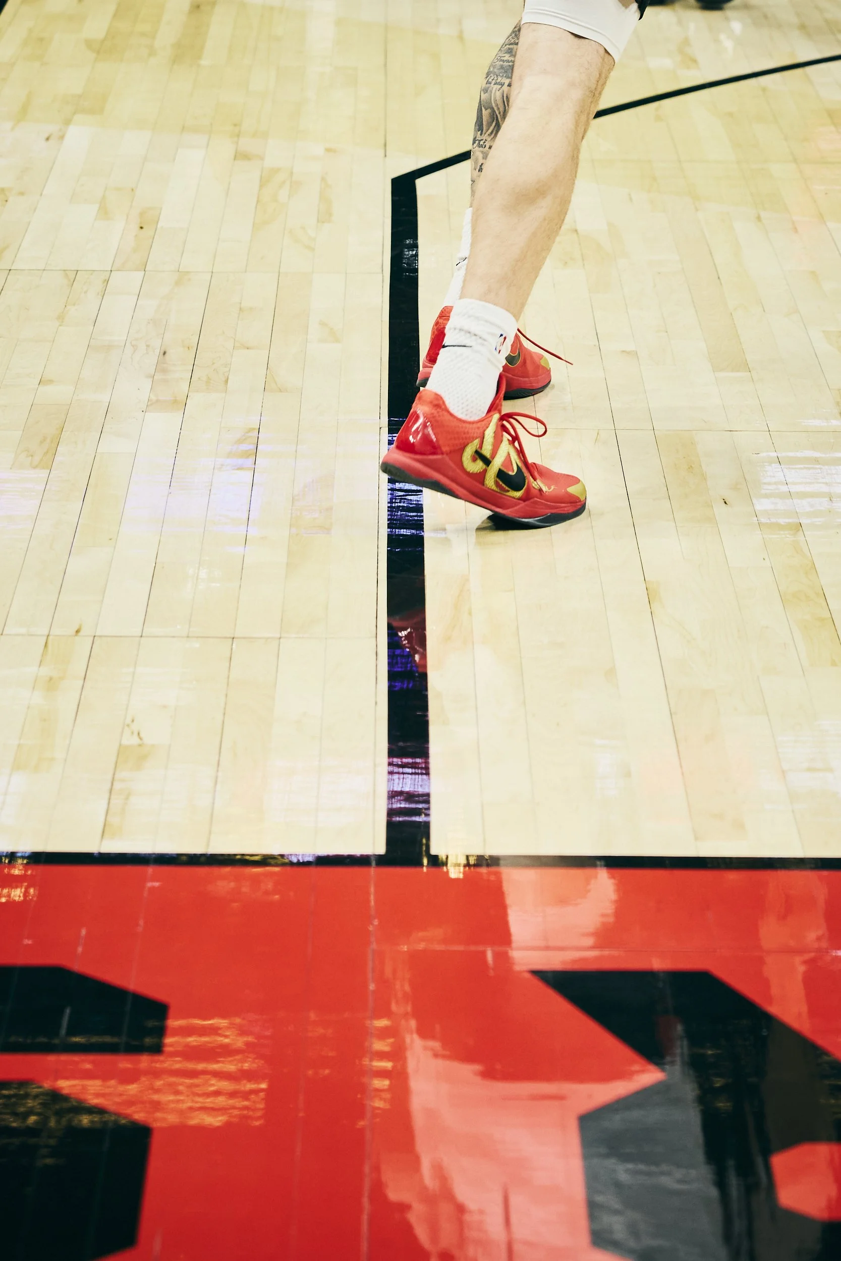 A basketball player wearing red Nike sneakers, white socks, and white shorts on a wooden basketball court.