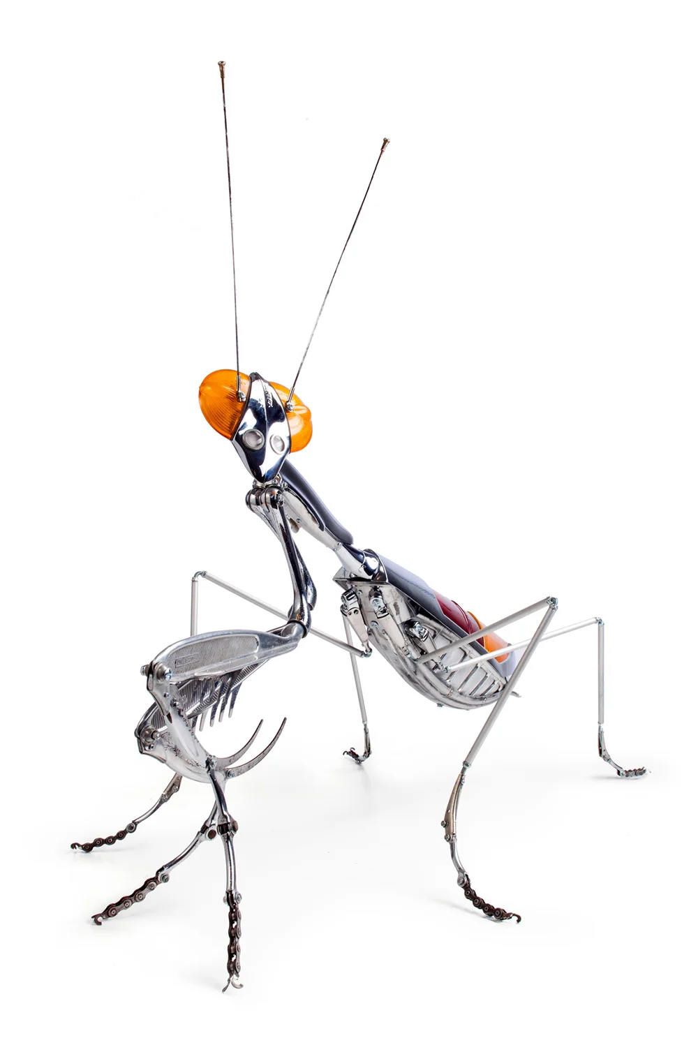 Praying Mantis , 104 x 50 x 74 centimetri. ADDOME: parafango bicicletta, ventilatore auto e parte di scarponi da sci; ALI: fanali posteriori di un Peugeot 404; TESTA: due indicatori del ciclomotore; TOP ARTI ANTERIORI: specchietti auto, affettatrici, schiaccianoci, pinze da spaghetti; PER TUTTE LE GAMBE: le estremità sono parti di freni della bici, più un po 'di catena della bici; ALTRE GAMBE: bracci del tergicristallo, tubi di alluminio; TORACE: paraurti e specchietti per auto.