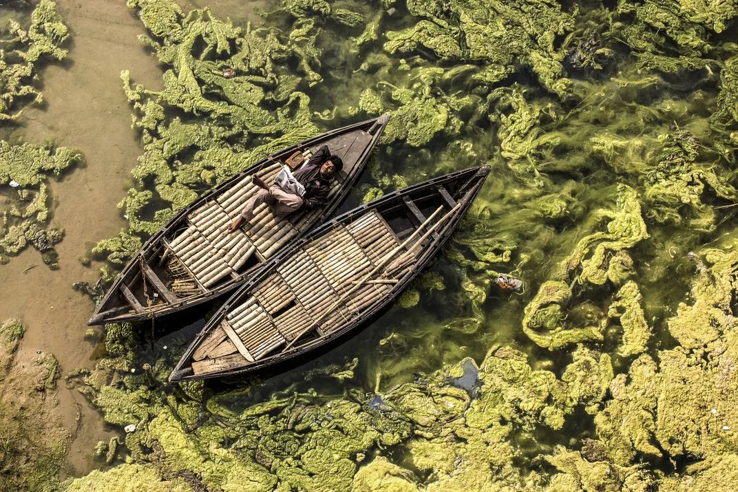 The Boatman, © Debashis Mukherjee. Un barcaiolo legge un giornale sulla sua barca