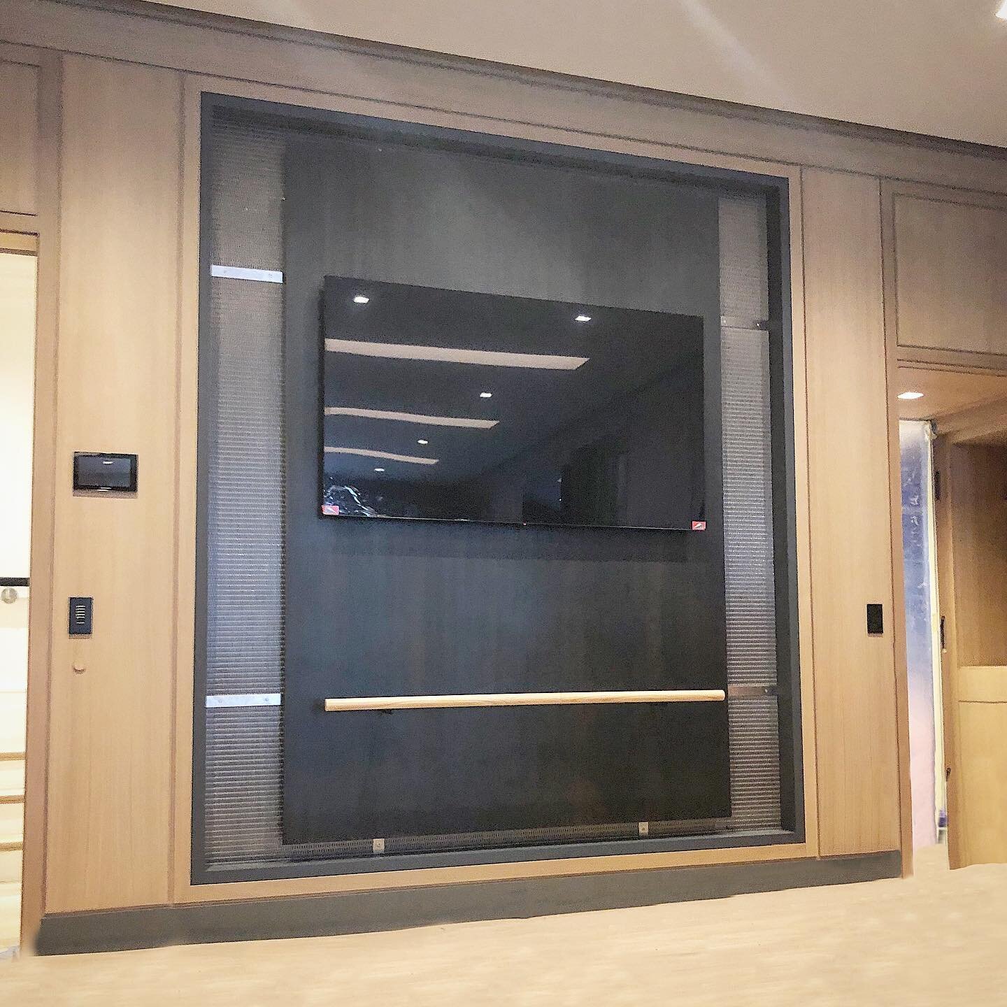 This framed niche with a woven stainless cloth backdrop pinned to the wall with brushed 1/8&rdquo; straps and countersunk screws holds an oversized floating 1/4&rdquo; blackened steel panel with integrated ballet bar and a 56&rdquo; TV. A gym like th